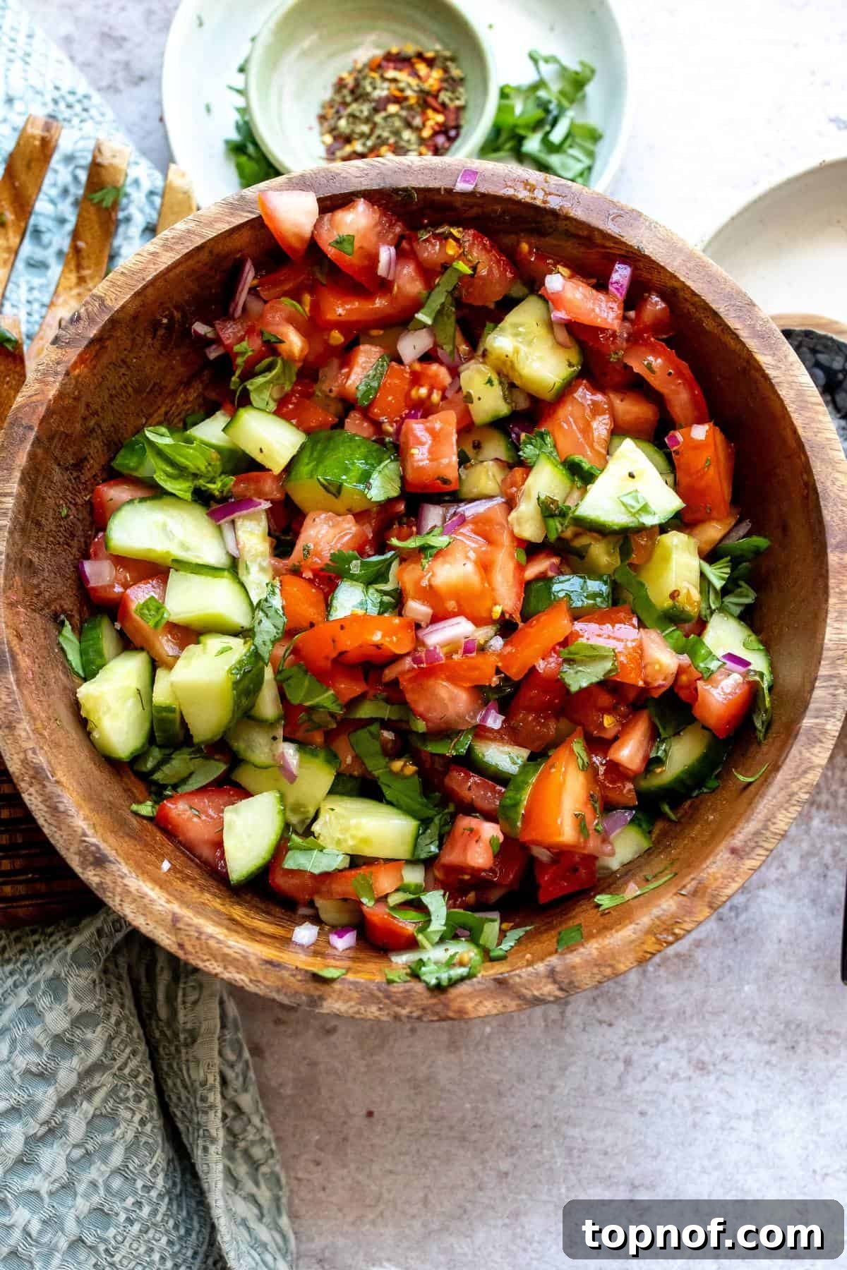 Garden Fresh Tomato Cucumber Salad 2 Wooden bowl filled with a vibrant Cucumber Tomato Salad, garnished with a sprinkle of red pepper flakes on the side.