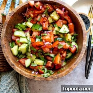 Wooden bowl with tomatoes and cucumber in it, red pepper flakes on the side.