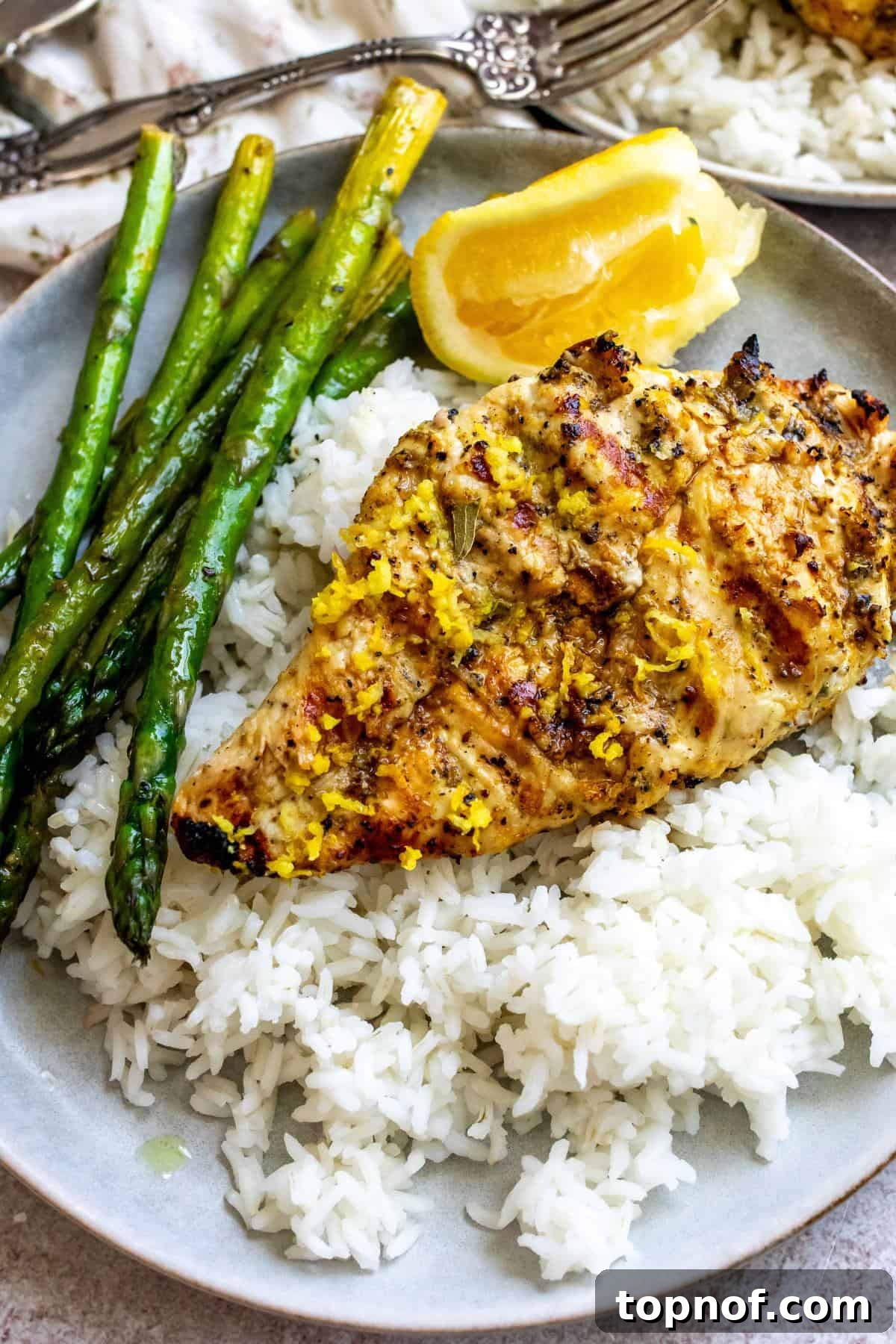 Peppery Citrus Chicken 5 Close-up photo of grey plates with lemon pepper chicken on rice, with squeezed lemon on the side.