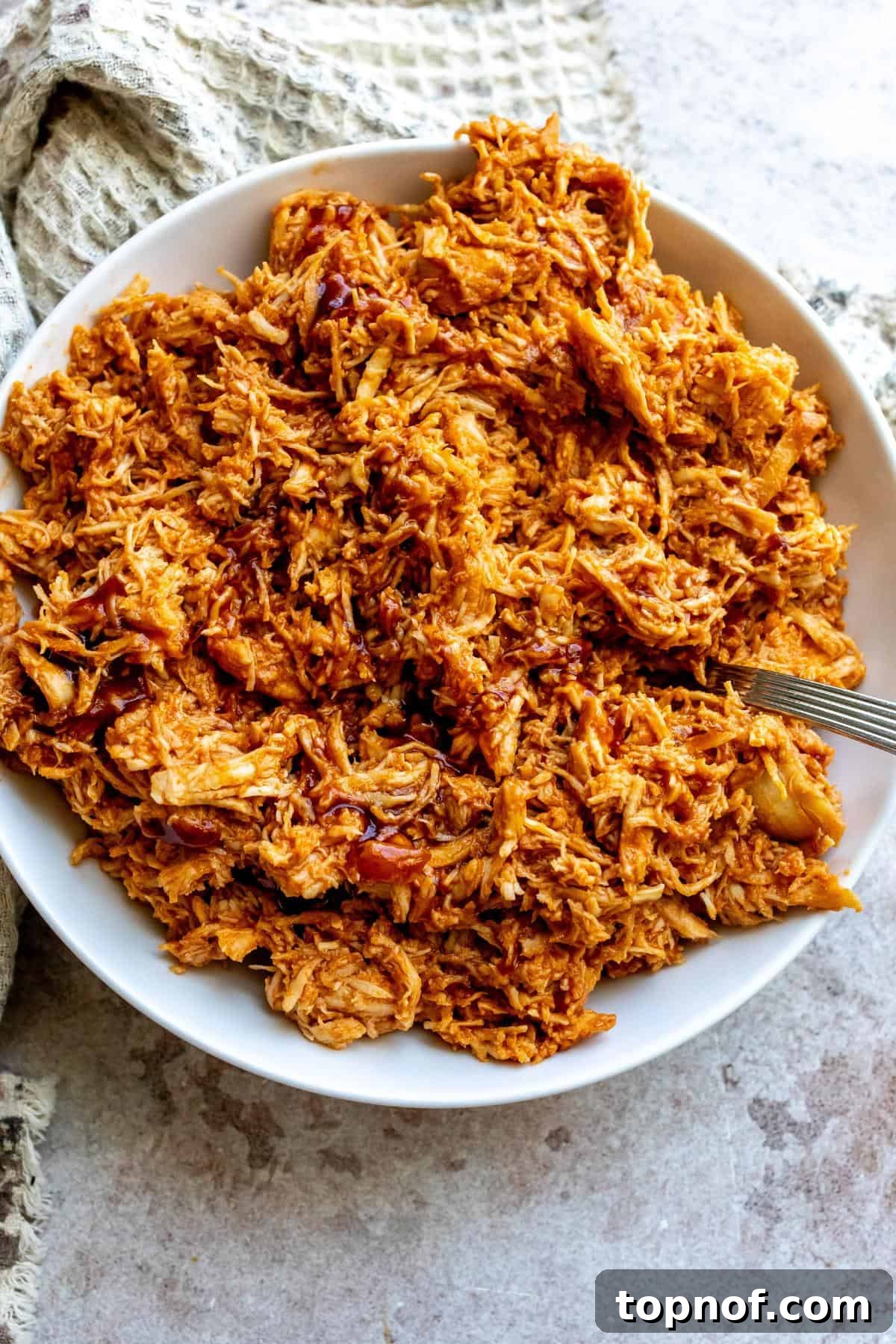 Slow-Smoked Pulled Chicken 2 An image of shredded BBQ chicken in a serving plate, garnished with fresh herbs.