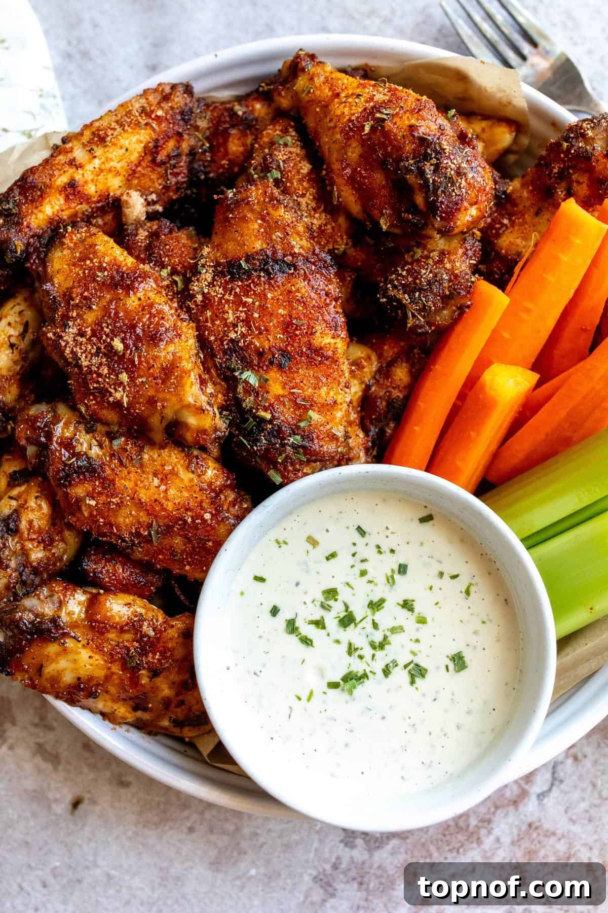 An overhead image of dry rub wings with a dipping sauce, carrot sticks and celery on the side, ready to be enjoyed.