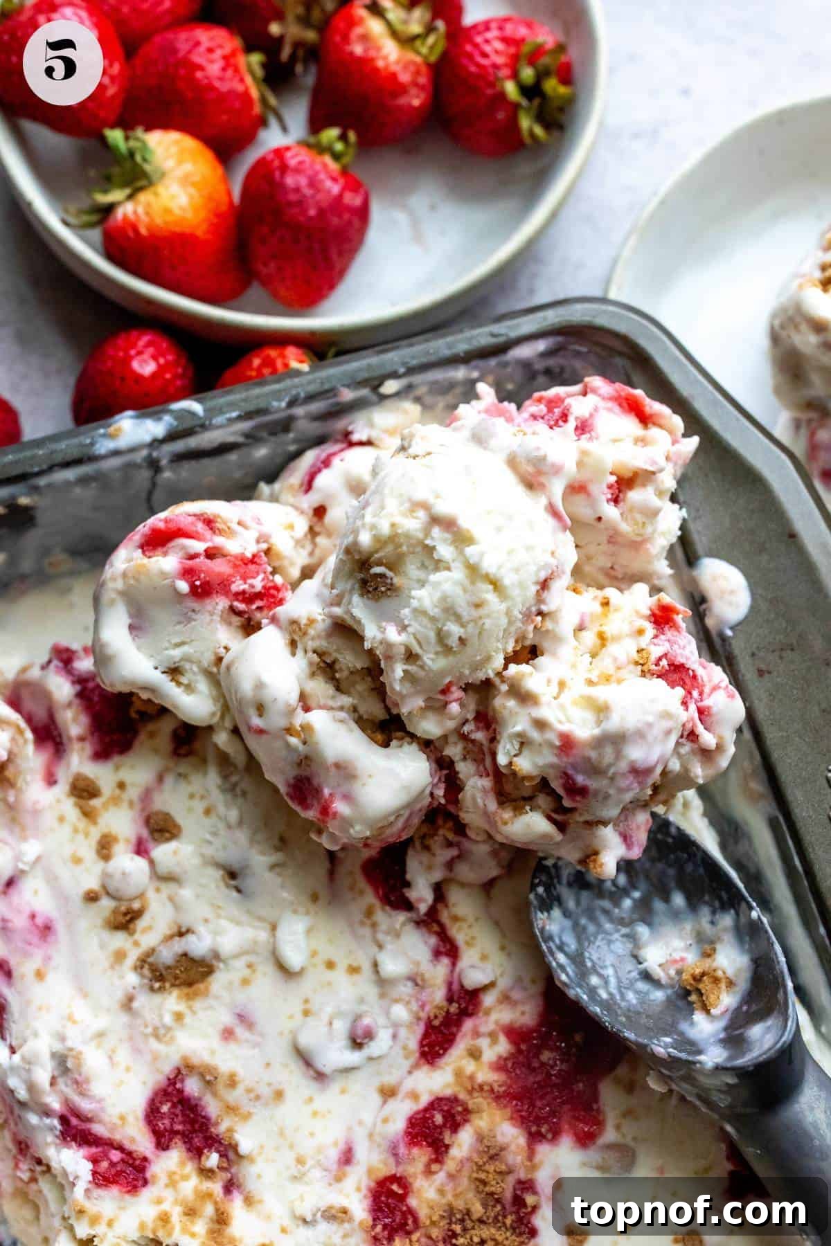 Homemade No-Churn Strawberry Cheesecake Indulgence 5 An image of scooping out strawberry cheesecake ice cream from the baking dish, showing visible swirls and crumbs.