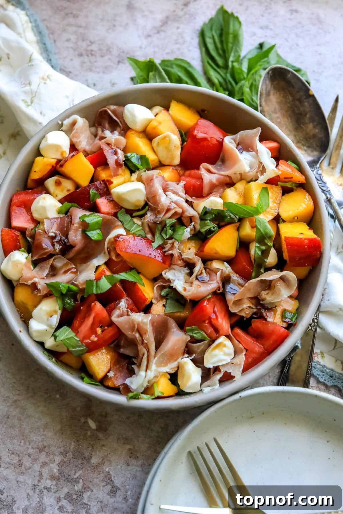 Overhead shot of peach caprese salad with basil and a spoon on the side, highlighting its fresh ingredients and vibrant colors.