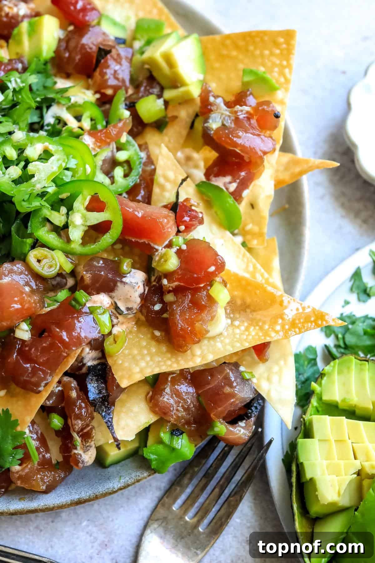 A close-up view of Tuna Poke Nachos on a plate with fresh toppings and sriracha aioli.