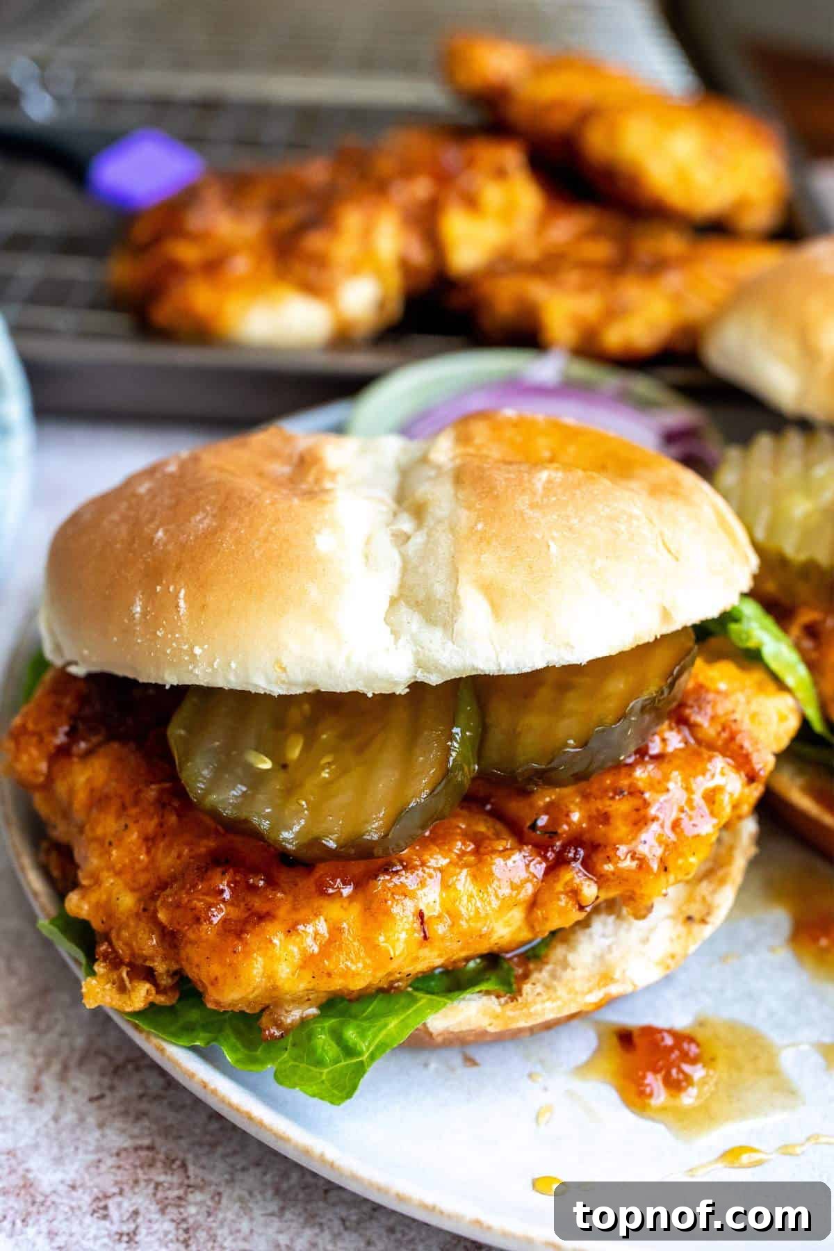 The Honey Blaze Chicken Sandwich 6 A fully assembled hot honey chicken sandwich, showcasing the crispy chicken, a generous drizzle of hot honey, and fresh toppings like pickles and onions on a toasted bun.