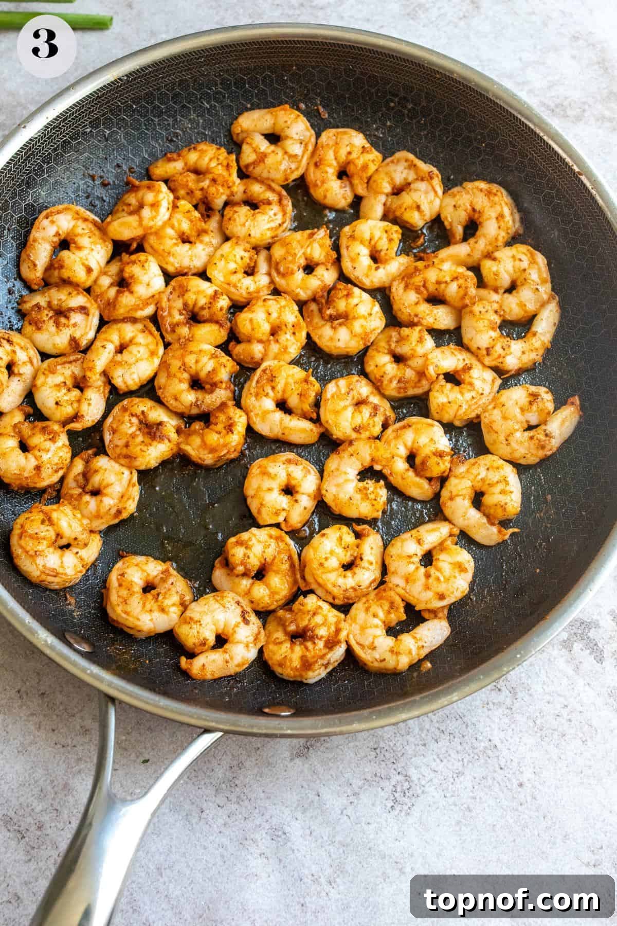 A close-up image of seasoned shrimp sizzling and turning pink in a hot skillet, indicating the cooking process.