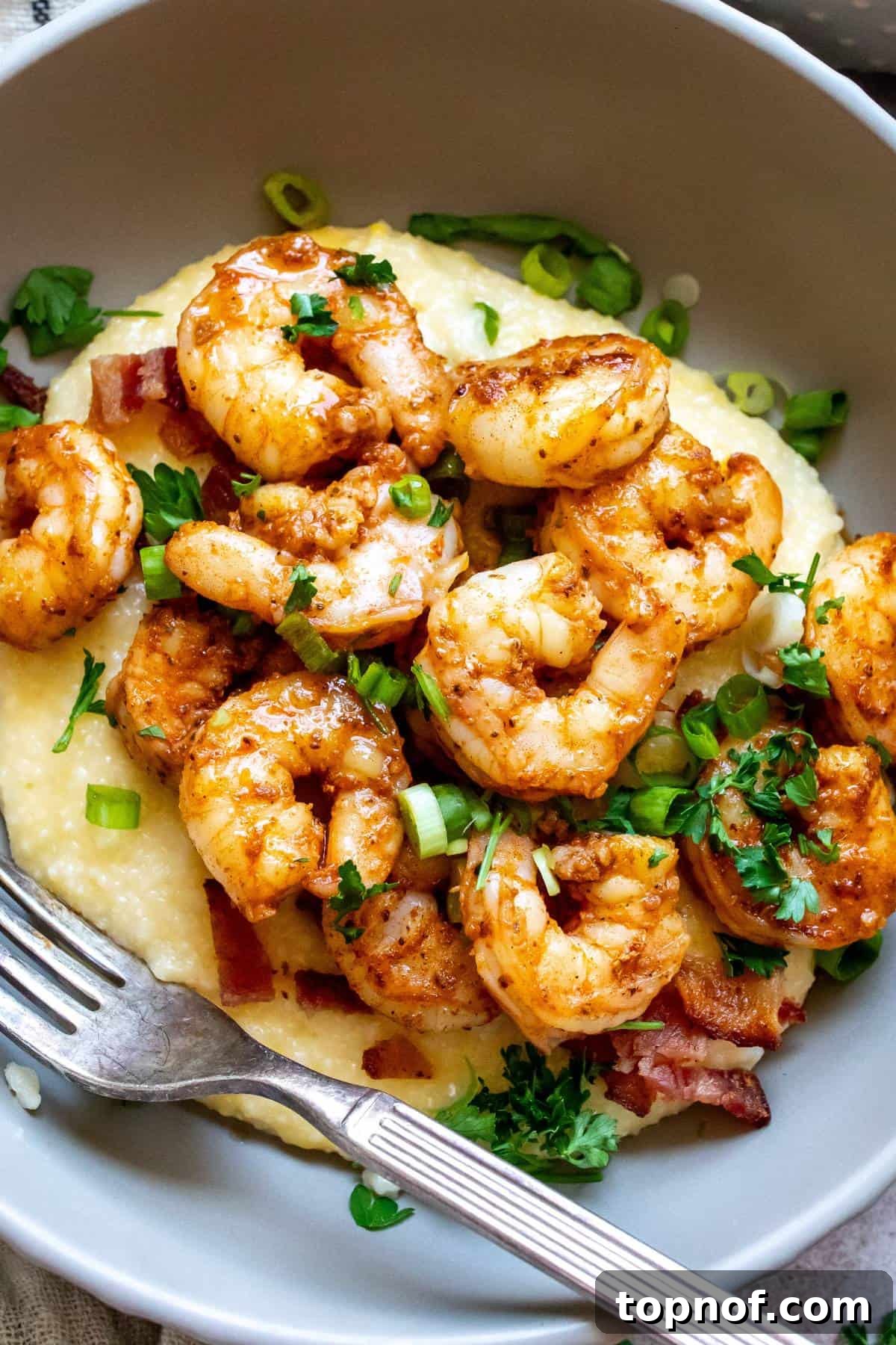 A mouth-watering close-up of perfectly cooked Cajun shrimp artfully arranged on a bed of creamy, cheesy grits, garnished and ready to serve.