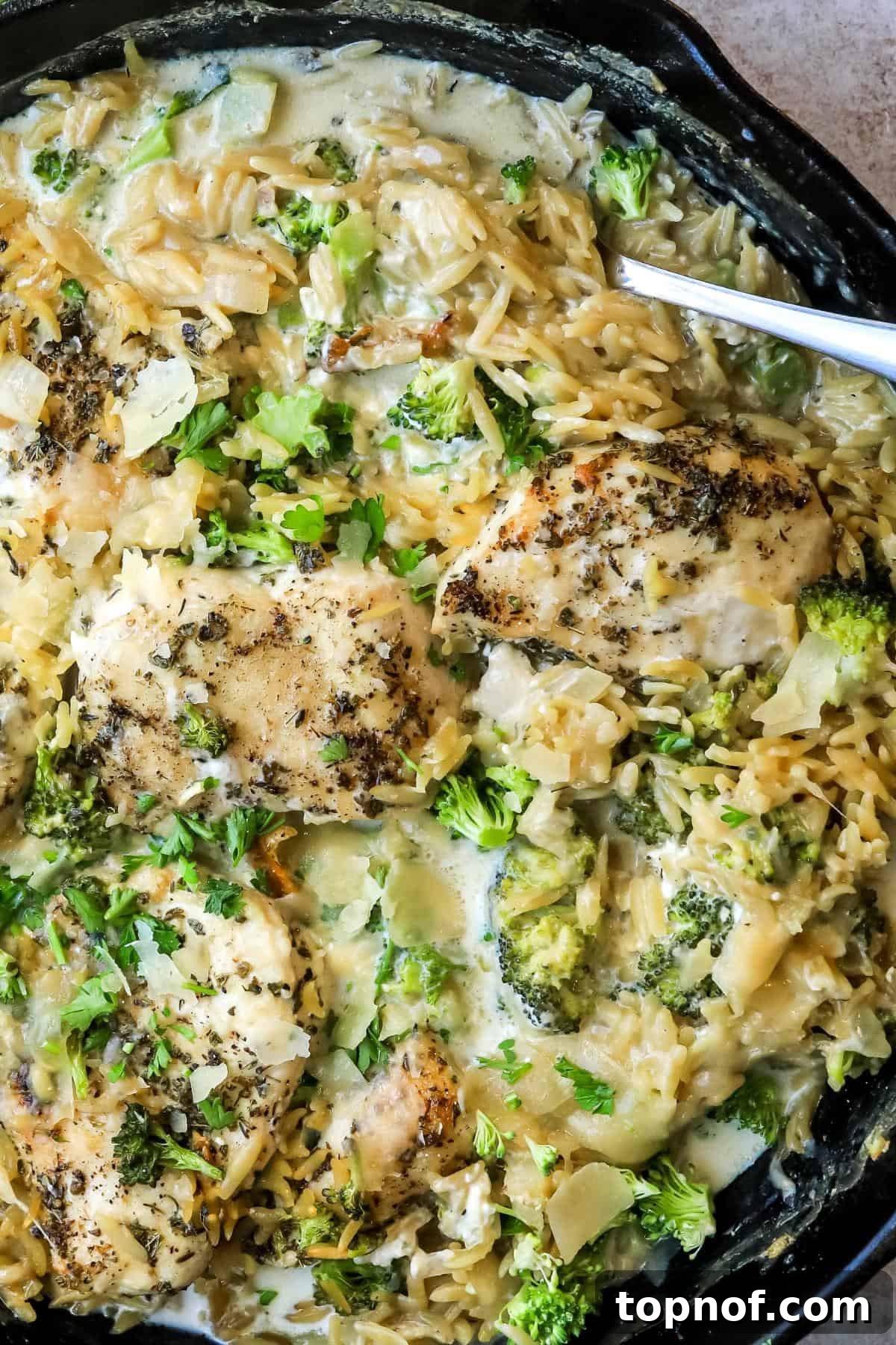 Close-up of Baked Chicken Alfredo Orzo in a cast iron pan, showing the creamy texture and golden-brown chicken, ready to be served.