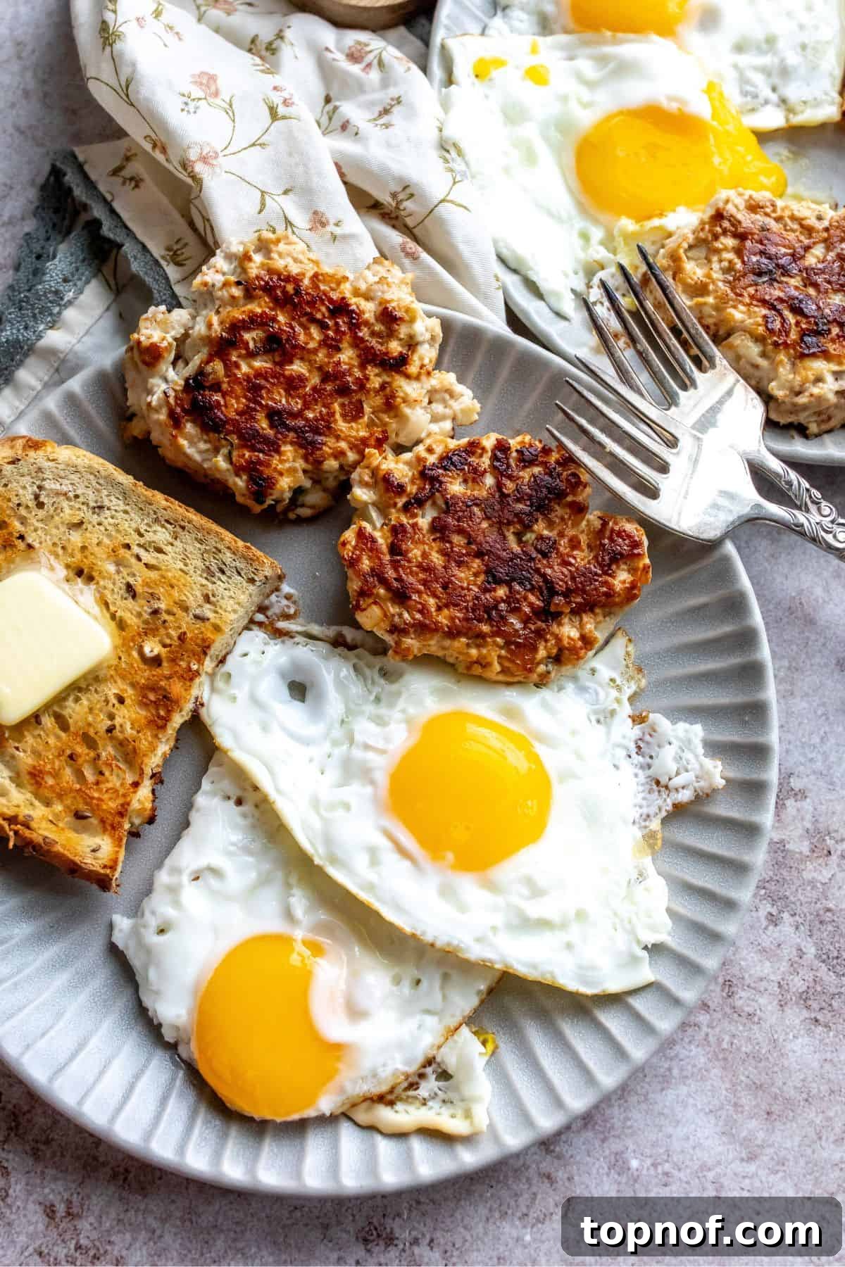 Two golden-brown chicken apple sausage patties served with two perfectly fried eggs and a slice of toasted whole wheat bread on a rustic plate, ready for a delicious breakfast.