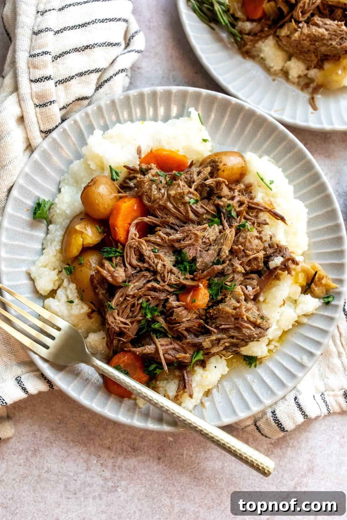Fall-Apart Tender Chuck Roast 2 An overhead image of a beef chuck roast recipe with potatoes and carrots on a plate, garnished with fresh herbs.