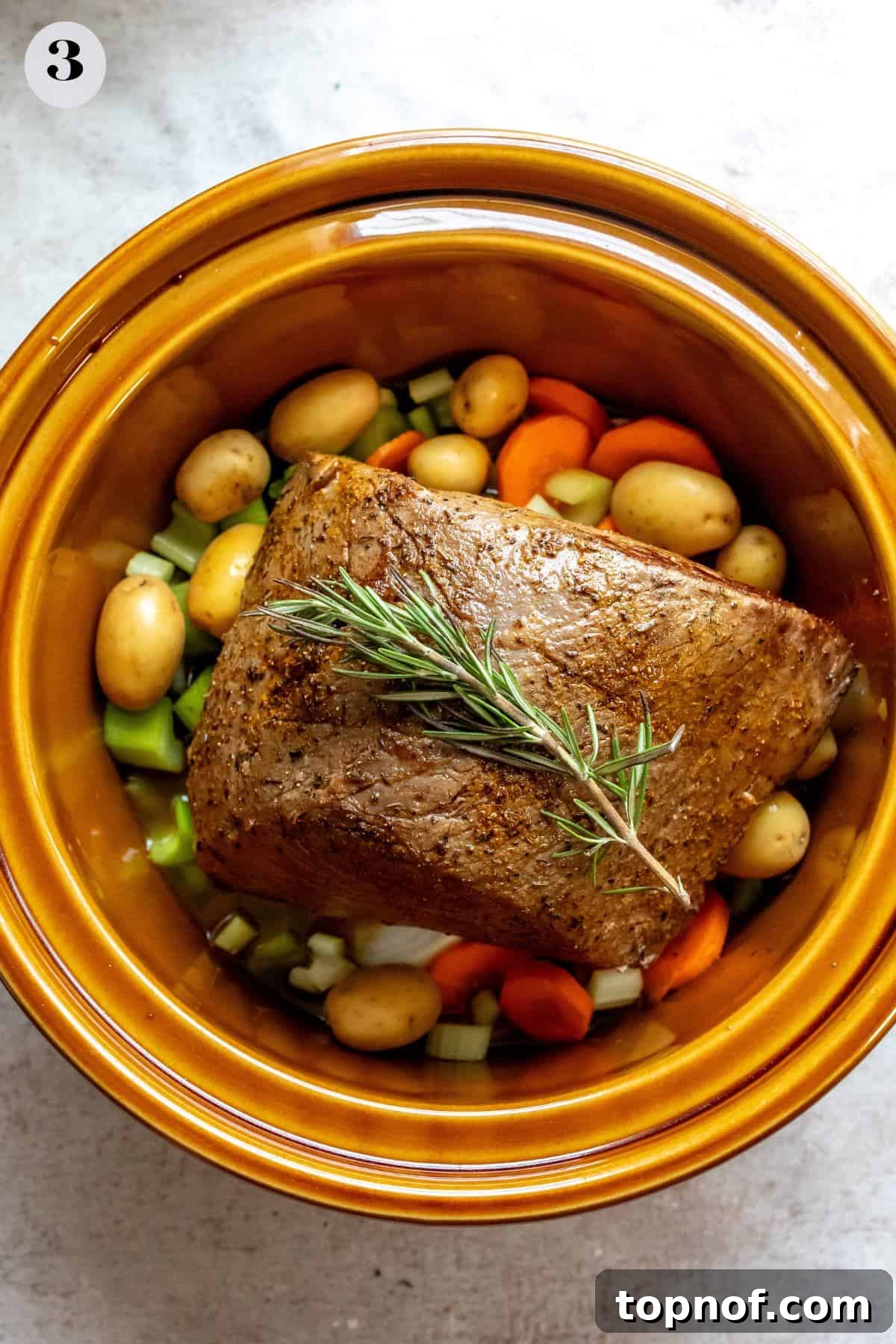 Fall-Apart Tender Chuck Roast 5 An image showing beef with carrots and potatoes simmering in a slow cooker, releasing rich aromas.