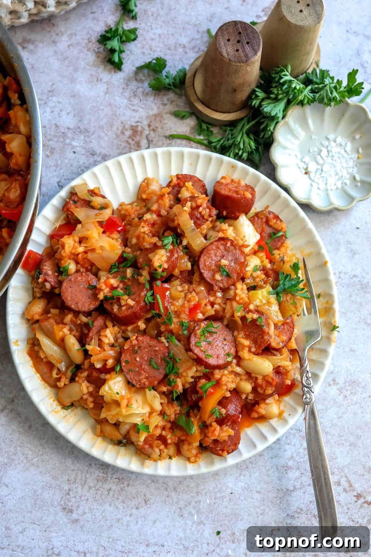 Ultimate Weeknight Slow Cooker Sausage Casserole 2 A white plate showcasing a generous serving of Slow Cooker Sausage Casserole, with a fork poised for enjoyment. The casserole features sliced sausage, colorful bell peppers, and other vegetables in a rich sauce.