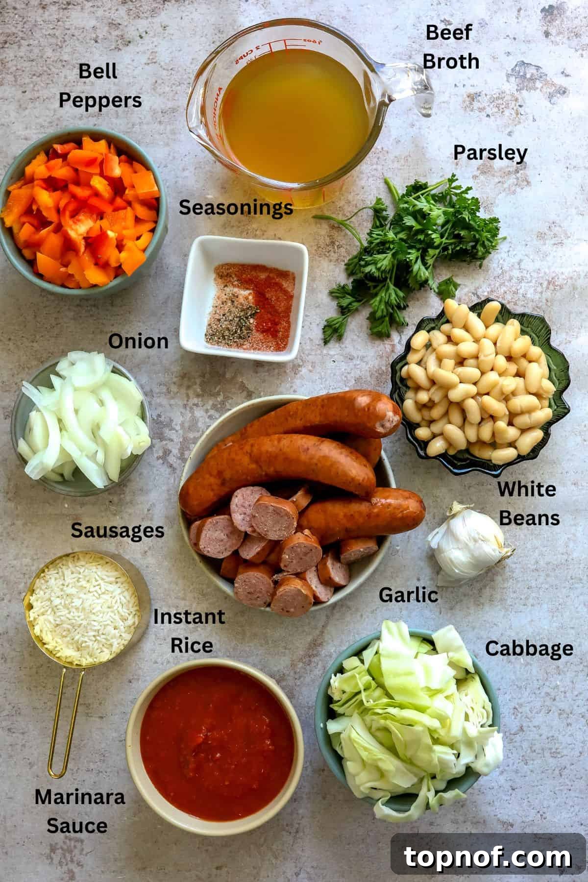 Ultimate Weeknight Slow Cooker Sausage Casserole 3 A collection of fresh ingredients laid out on a kitchen counter, including sliced sausages, colorful bell peppers, onions, garlic, broth, marinara sauce, and cabbage, ready for cooking.