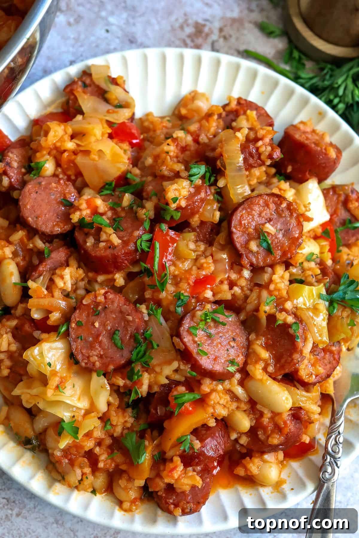 Ultimate Weeknight Slow Cooker Sausage Casserole 5 A close-up view of a white plate filled with Slow Cooker Sausage Casserole, showcasing the texture of the sausage, vegetables, and rice, with a fork resting beside it.