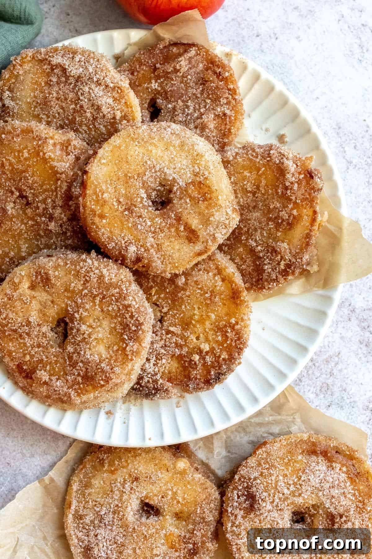 Warm Apple Cinnamon Doughnuts 5 An overhead image of a stack of freshly fried, cinnamon sugar-coated apple donuts on a plate.