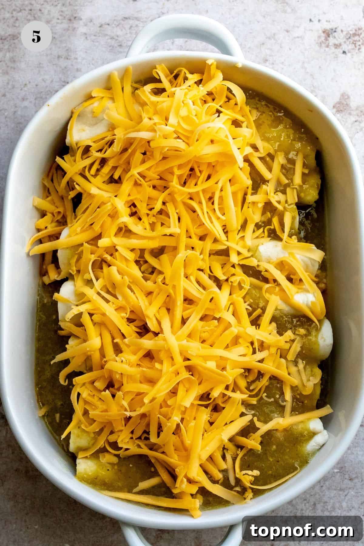 Breakfast Enchilada Casserole 5 White casserole dish with enchiladas and shredded cheese.