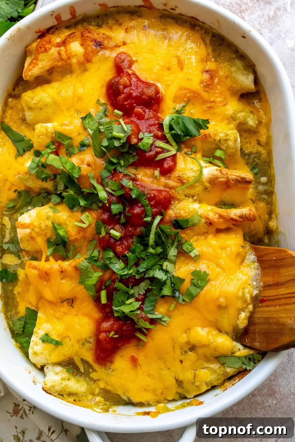 Breakfast Enchilada Casserole 6 White casserole dish with Breakfast Enchiladas in it and wooden spatula.