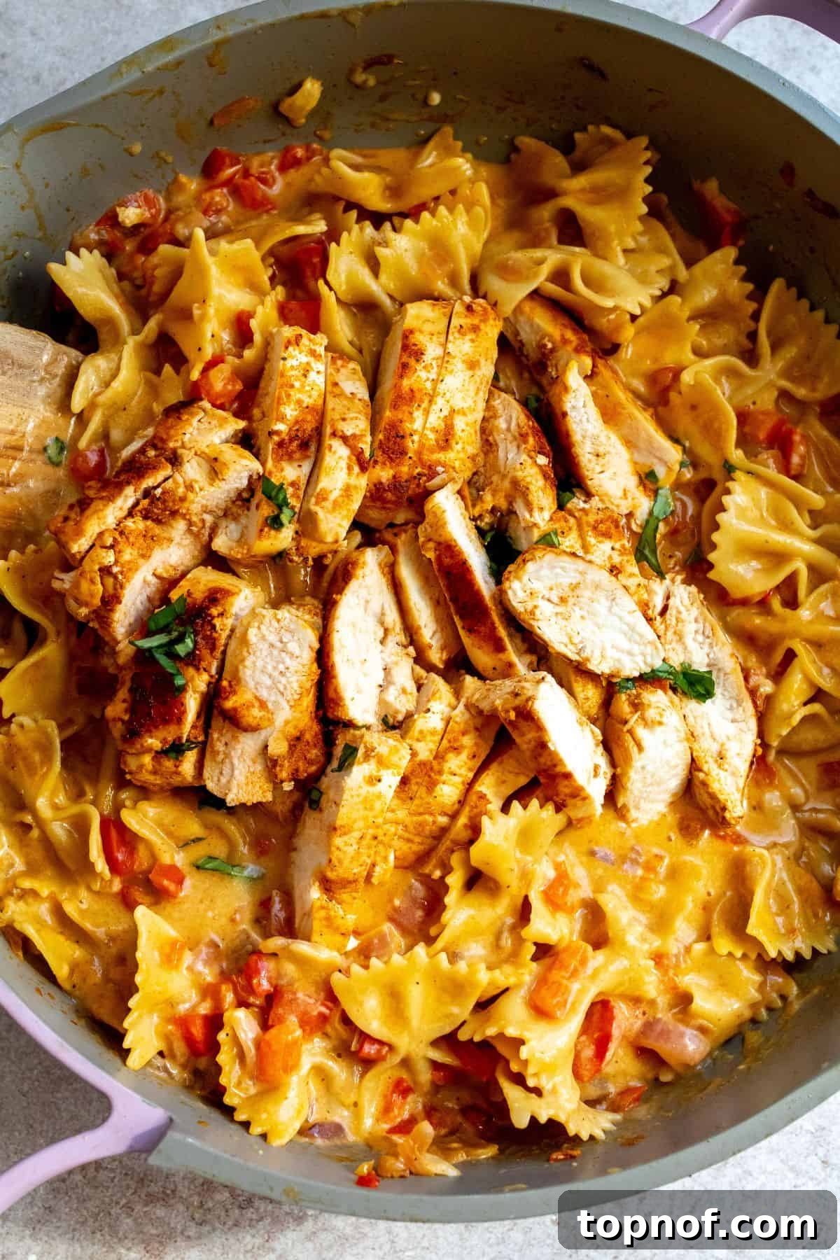 Tex-Mex Chicken Fajita Pasta 2 Close-up of One-Pan Creamy Chicken Fajita Pasta in a grey and pink skillet with a wooden spatula, showcasing rich colors and creamy sauce.
