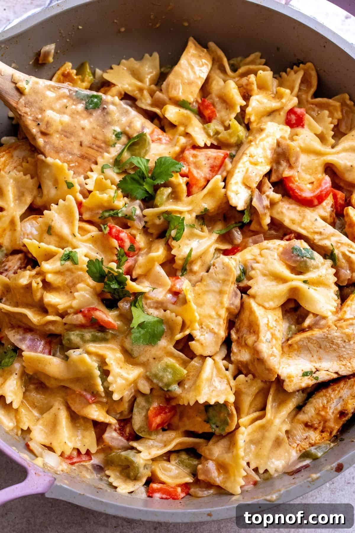 Tex-Mex Chicken Fajita Pasta 5 Close-up view of Chicken Fajita Pasta served in a grey and pink skillet with a wooden spatula, highlighting the creamy texture.