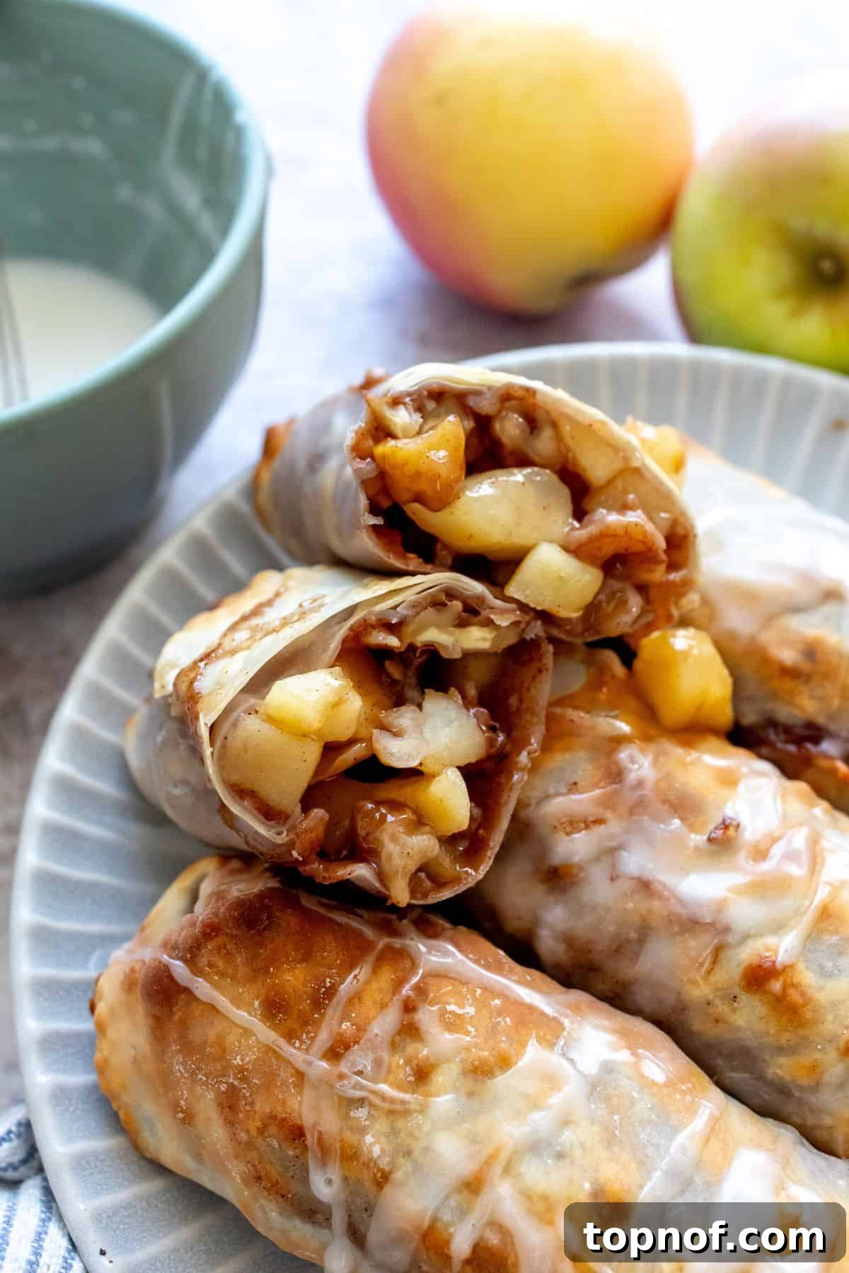 Crispy Apple Pie Rolls 2 Crispy apple pie egg rolls on a plate with icing, showcasing their golden-brown perfection.