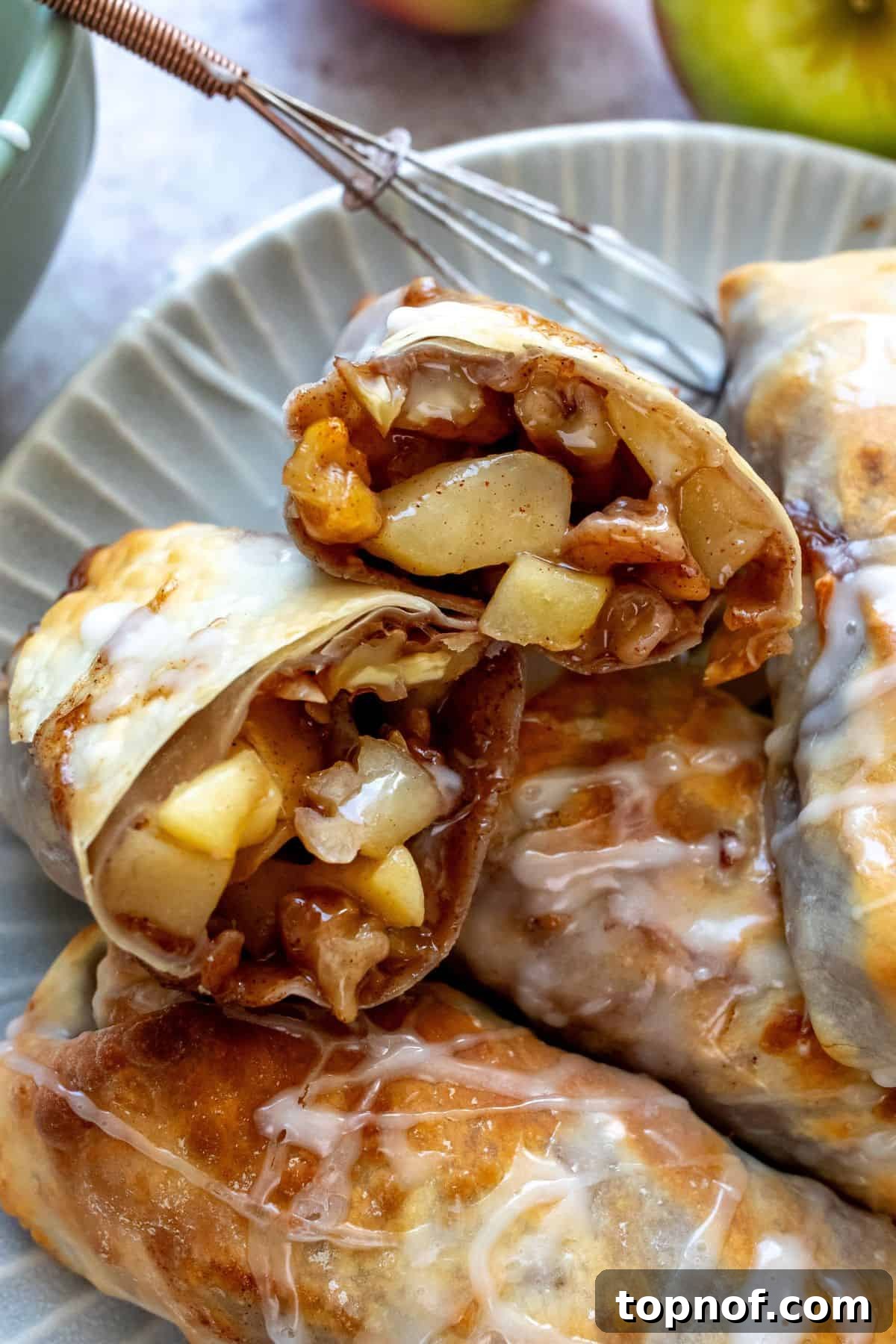 Crispy Apple Pie Rolls 5 Close-up view of crispy apple pie egg rolls on a white plate, beautifully drizzled with icing.