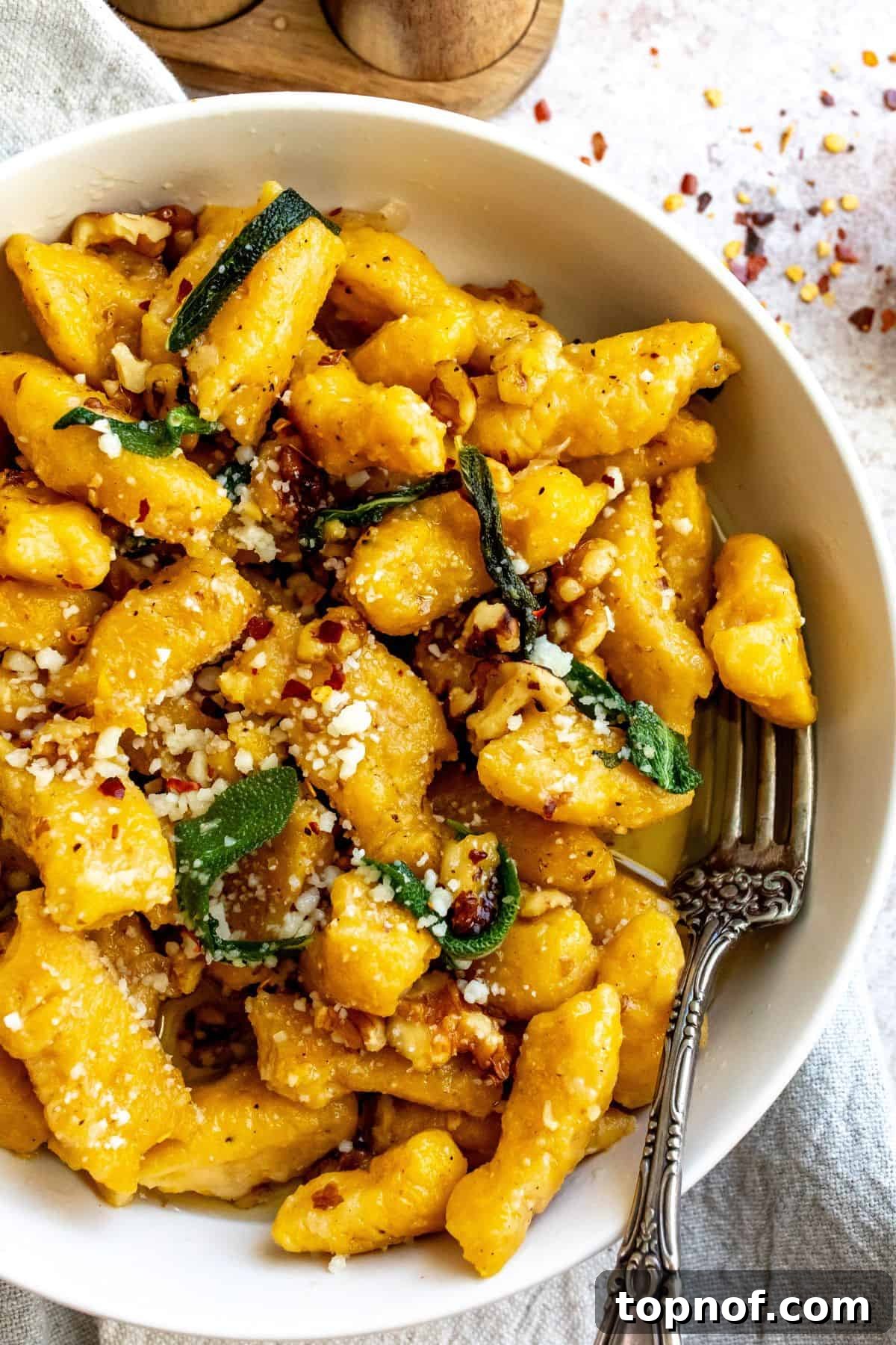 A close-up image of tender butternut squash gnocchi coated in a creamy brown butter sauce, garnished with fresh sage and walnuts.