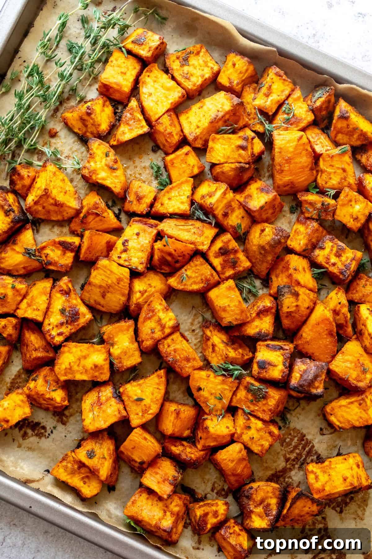 Crispy Baked Sweet Potatoes 5 A parchment-lined baking sheet showcasing perfectly roasted crispy sweet potatoes, golden and tender, with a scattering of fresh thyme leaves for garnish.