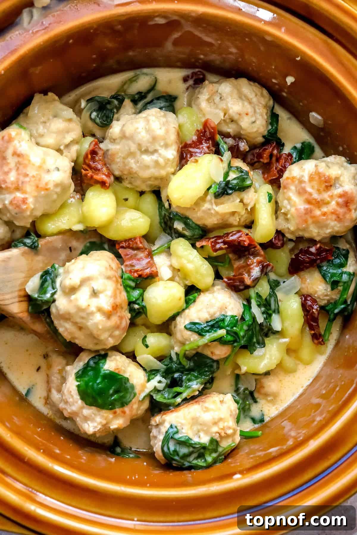 Creamy Slow Cooker Tuscan Chicken Meatball Gnocchi 5 Close-up shot of Slow Cooker Tuscan Chicken Meatballs with Gnocchi simmering in a brown crockpot, showing its creamy texture and rich ingredients.