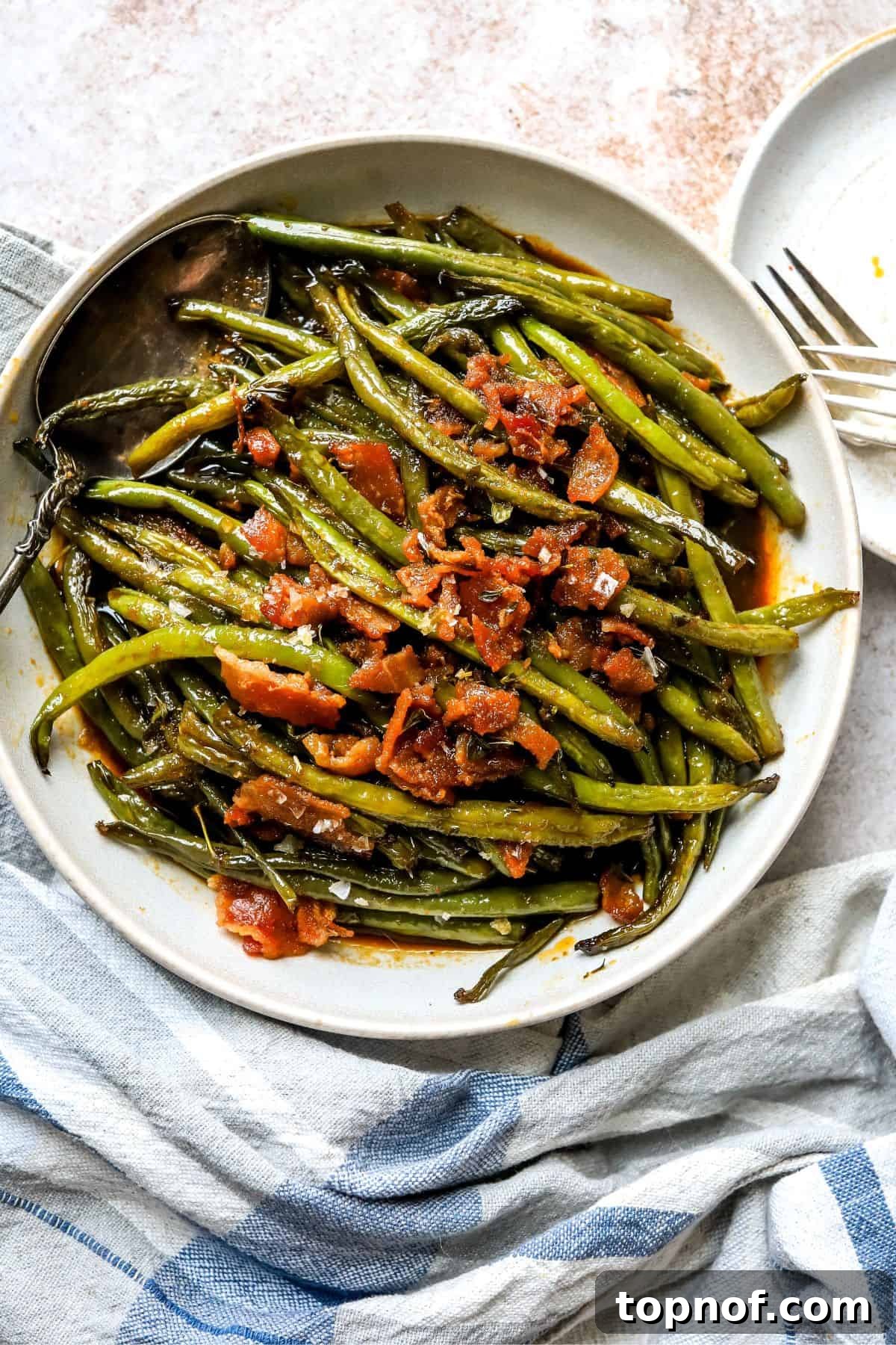 An overhead image of crack green beans on a plate, with golden-brown crispy bacon bits on top, ready to be served.