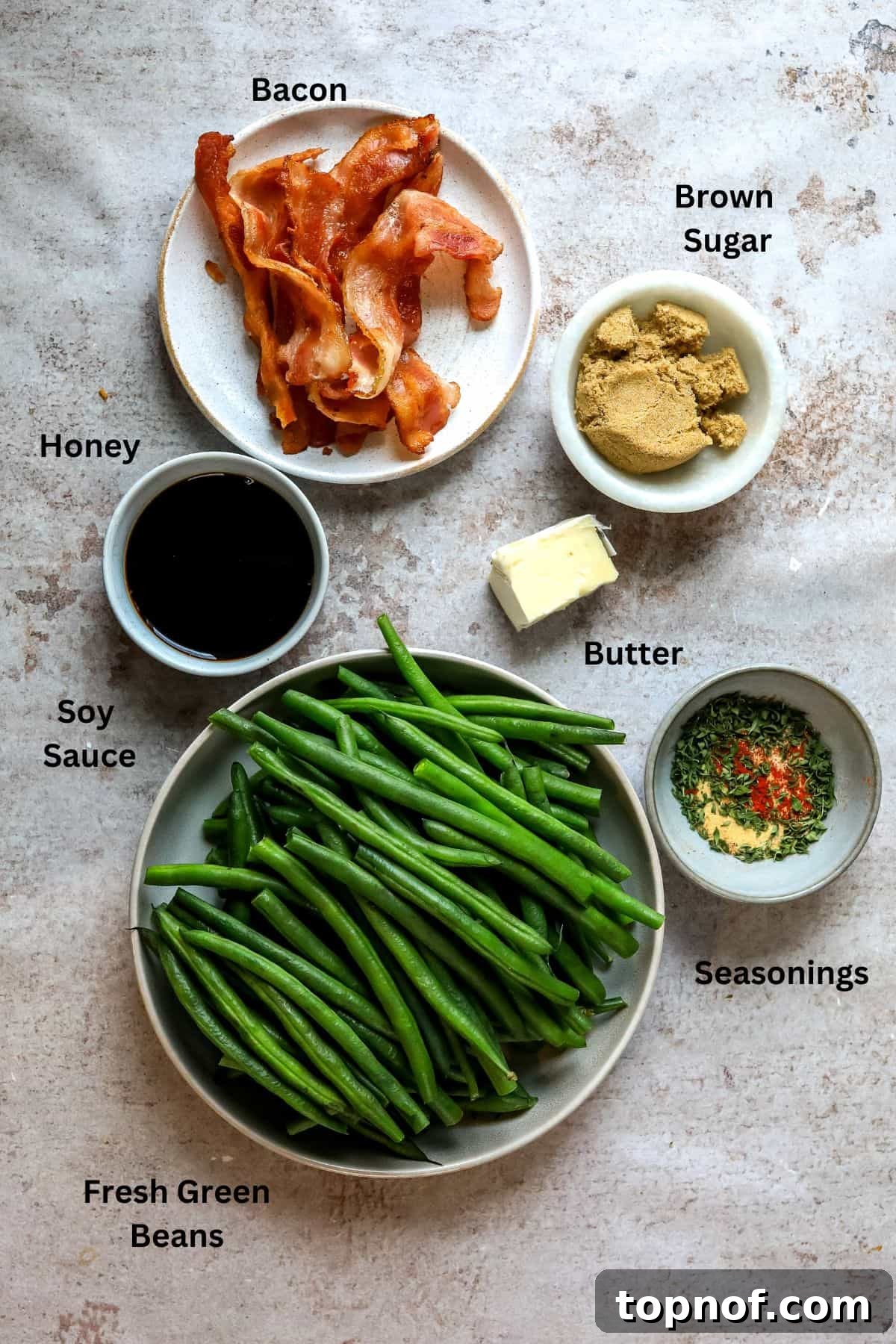 Snappy Green Beans 3 An overhead image showing all the fresh ingredients laid out for making crack green beans, including vibrant green beans, strips of bacon, butter, honey, soy sauce, brown sugar, and various spices.