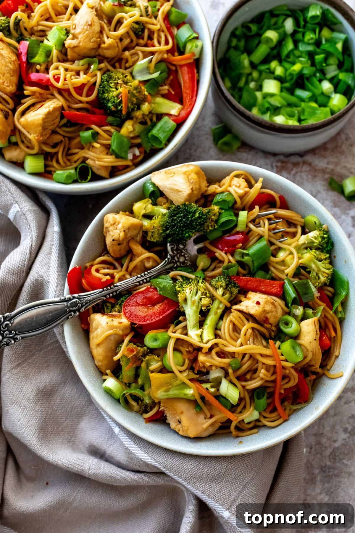 Savory Teriyaki Chicken Ramen Bowl 2 A grey bowl filled with homemade Teriyaki Chicken Ramen, featuring tender chicken, bright green broccoli, and red bell peppers, with a striped dish towel placed beside it.