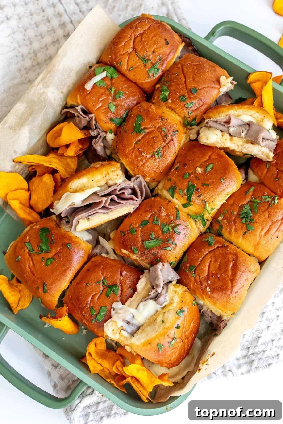 Premium Roast Beef Minis 2 Golden brown roast beef sliders in a green baking pan, served with sweet potato chips on the side, ready to be enjoyed.