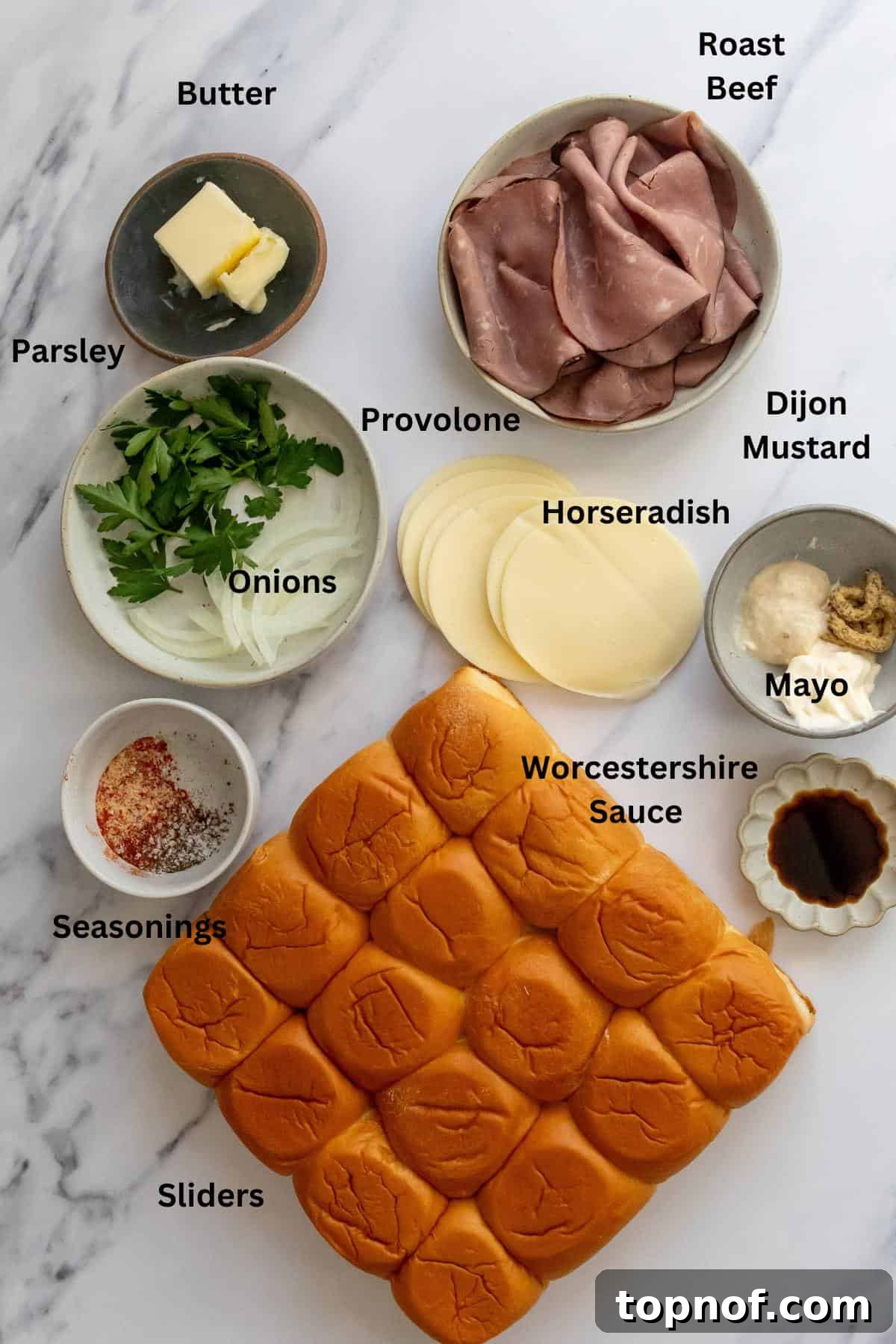 Premium Roast Beef Minis 3 Various ingredients for roast beef sliders laid out in small bowls on a clean white counter, showcasing fresh and prepared items.