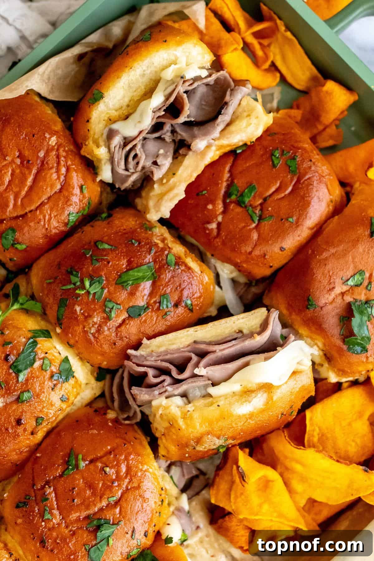 Premium Roast Beef Minis 5 A close-up shot of baked roast beef sliders on parchment paper, showing the melted cheese and golden-brown tops.