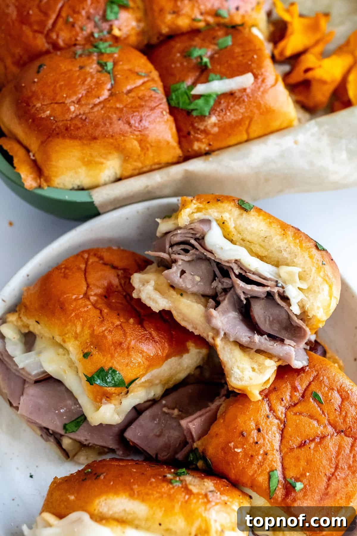 Premium Roast Beef Minis 6 A plate of golden-brown roast beef sliders garnished with fresh parsley and showing melted cheese, ready to be served.