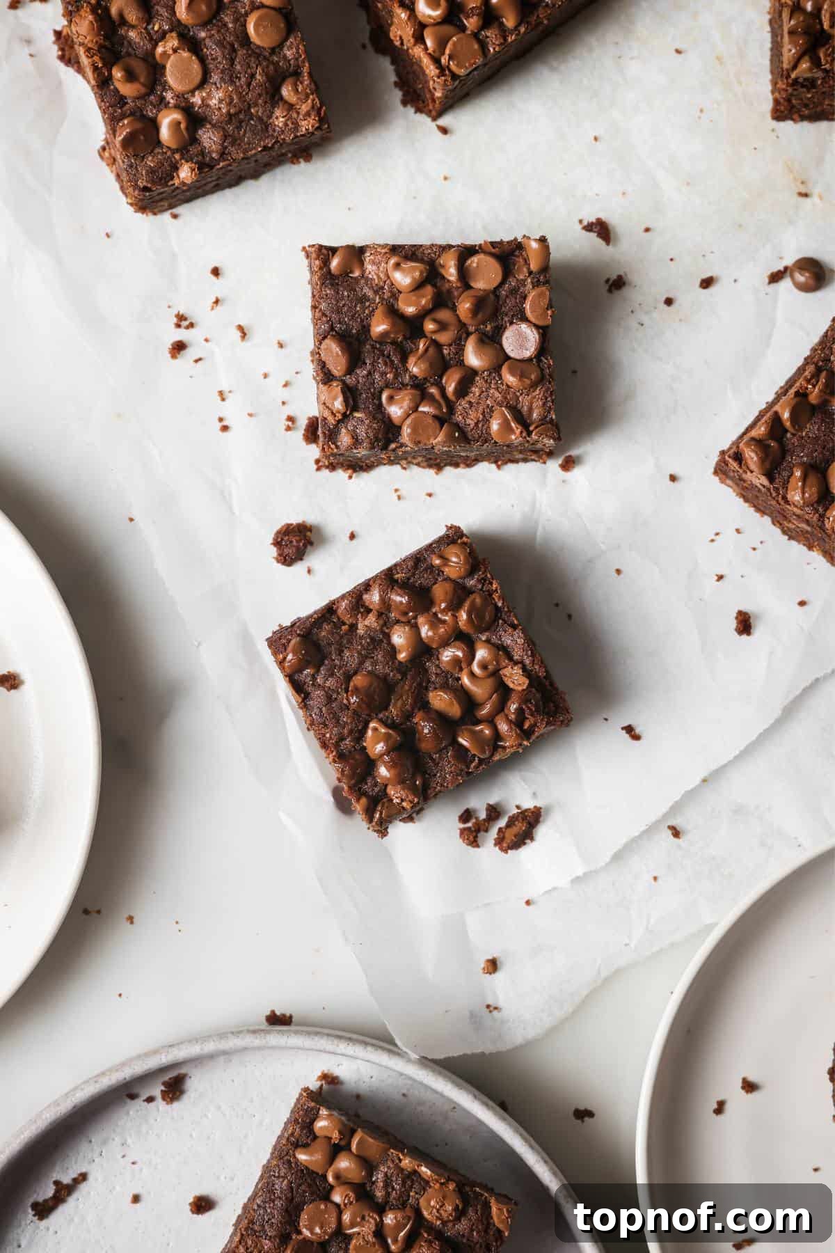 Double Chocolate Chip Cookie Bars 2 Decadent Chocolate Chocolate Chip Cookie Bars presented on elegant white parchment paper, ready to be served, with clean plates nearby.