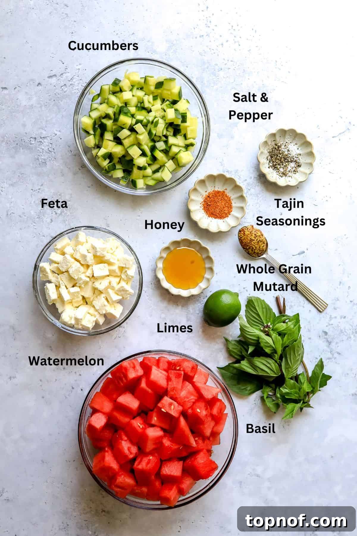 Watermelon Basil Bliss 3 A flat lay shot showcasing all the fresh ingredients for Watermelon Feta Salad – cubed watermelon, cucumber slices, crumbled feta, fresh basil, and limes, on a grey countertop.