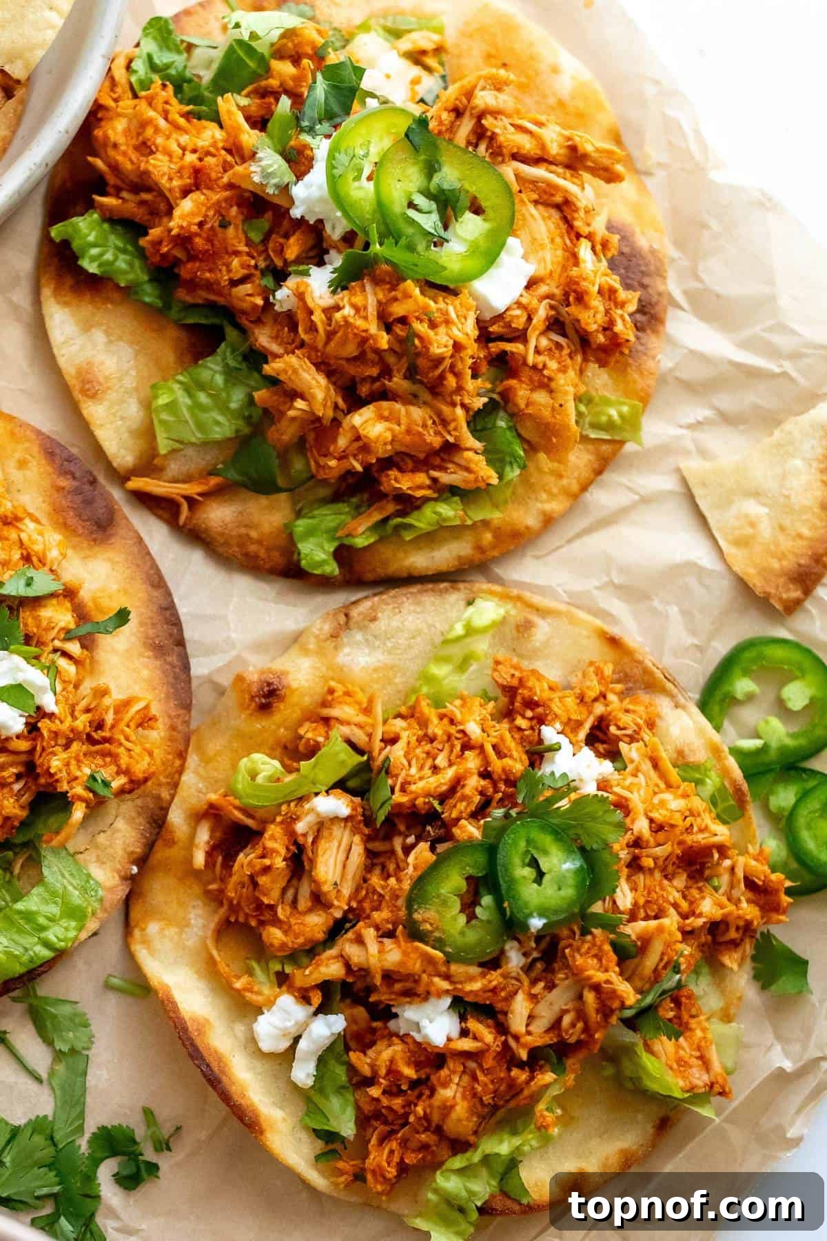 Smoky Chicken Tinga Tostadas 6 Close-up shot of a beautifully assembled Chicken Tinga Tostada, garnished with fresh jalapeños and cilantro on parchment paper.
