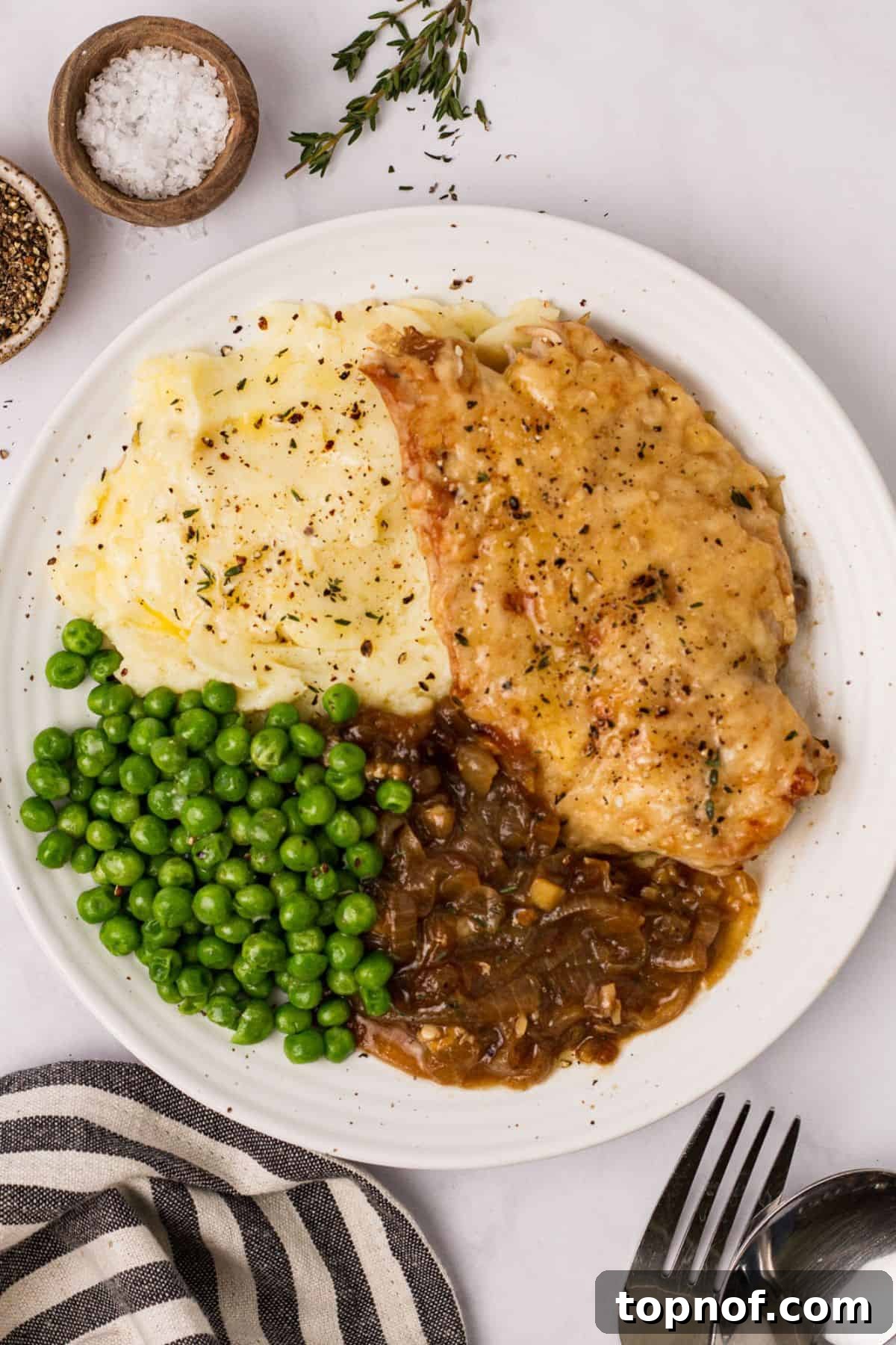 Caramelized Onion Chicken Au Gratin 2 White ceramic plate with French onion soup chicken and peas and a fork to the side, showcasing a delicious and comforting meal.