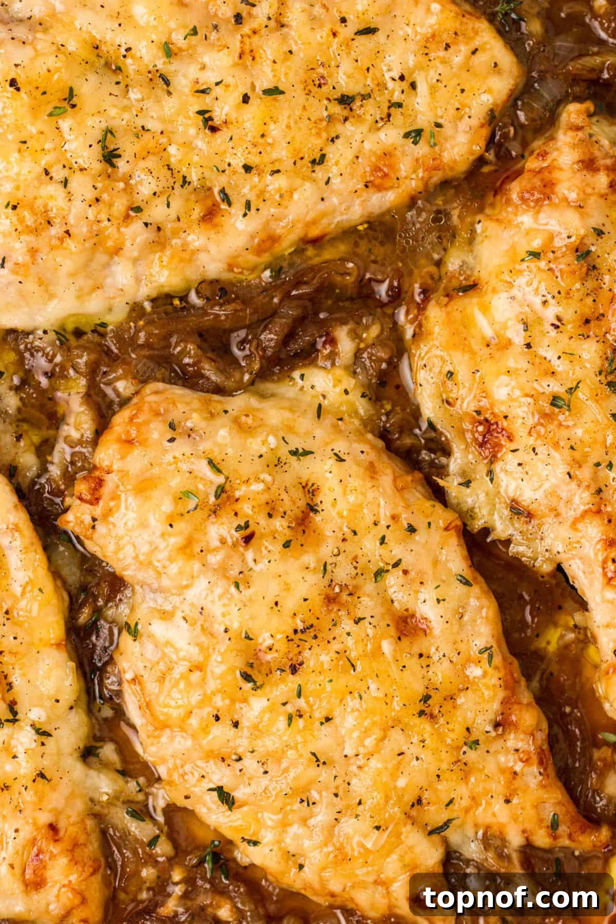Caramelized Onion Chicken Au Gratin 6 Up close photo of French Onion Soup Chicken in sauce, topped with melted and golden Gruyère cheese, served on a white plate.
