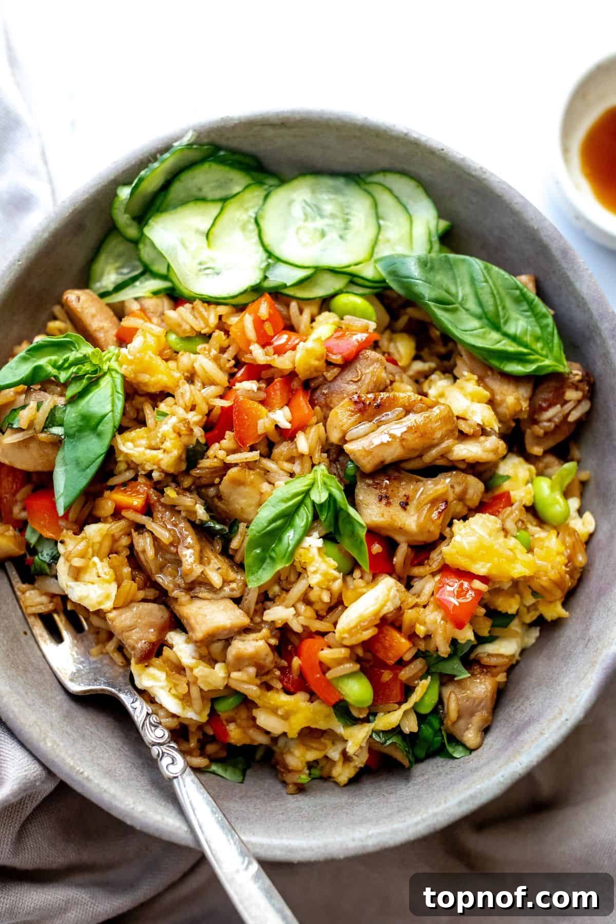 Grey ceramic bowl with Thai Basil Chicken Fried Rice in it and fresh cucumbers to the side. 
