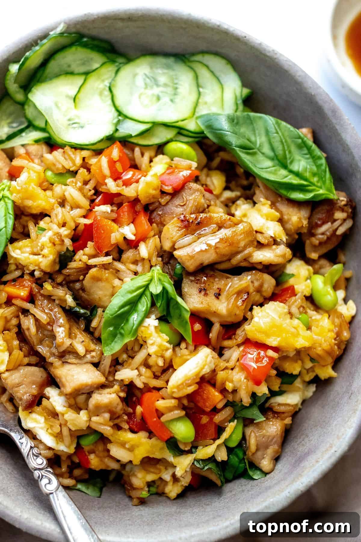 Grey ceramic bowl with Thai Basil Chicken Fried Rice in it and fresh cucumbers to the side. 