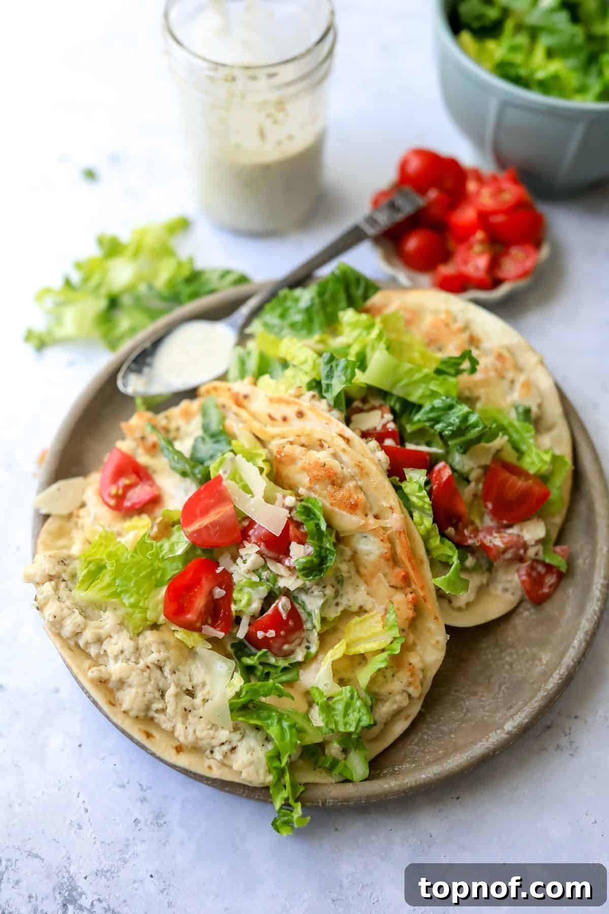 Caesar Chicken Smash Tacos 2 Delicious Chicken Caesar Smashed Tacos served elegantly on a grey plate with a side of creamy Caesar dressing and a spoon for garnish.