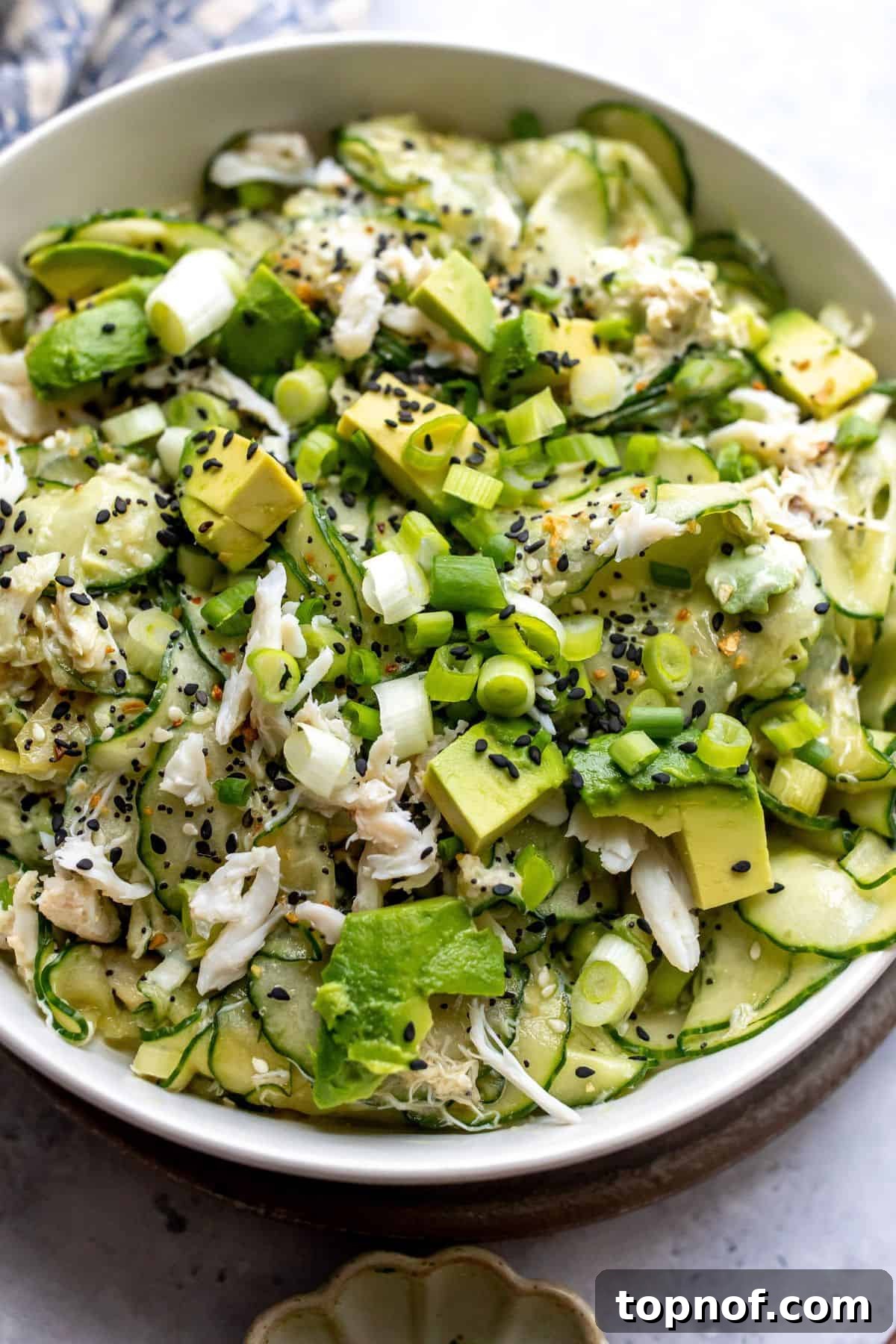 California Roll Cucumber Slaw 2 White bowl filled with California Roll Cucumber Salad. Avocados on top with sesame seeds.