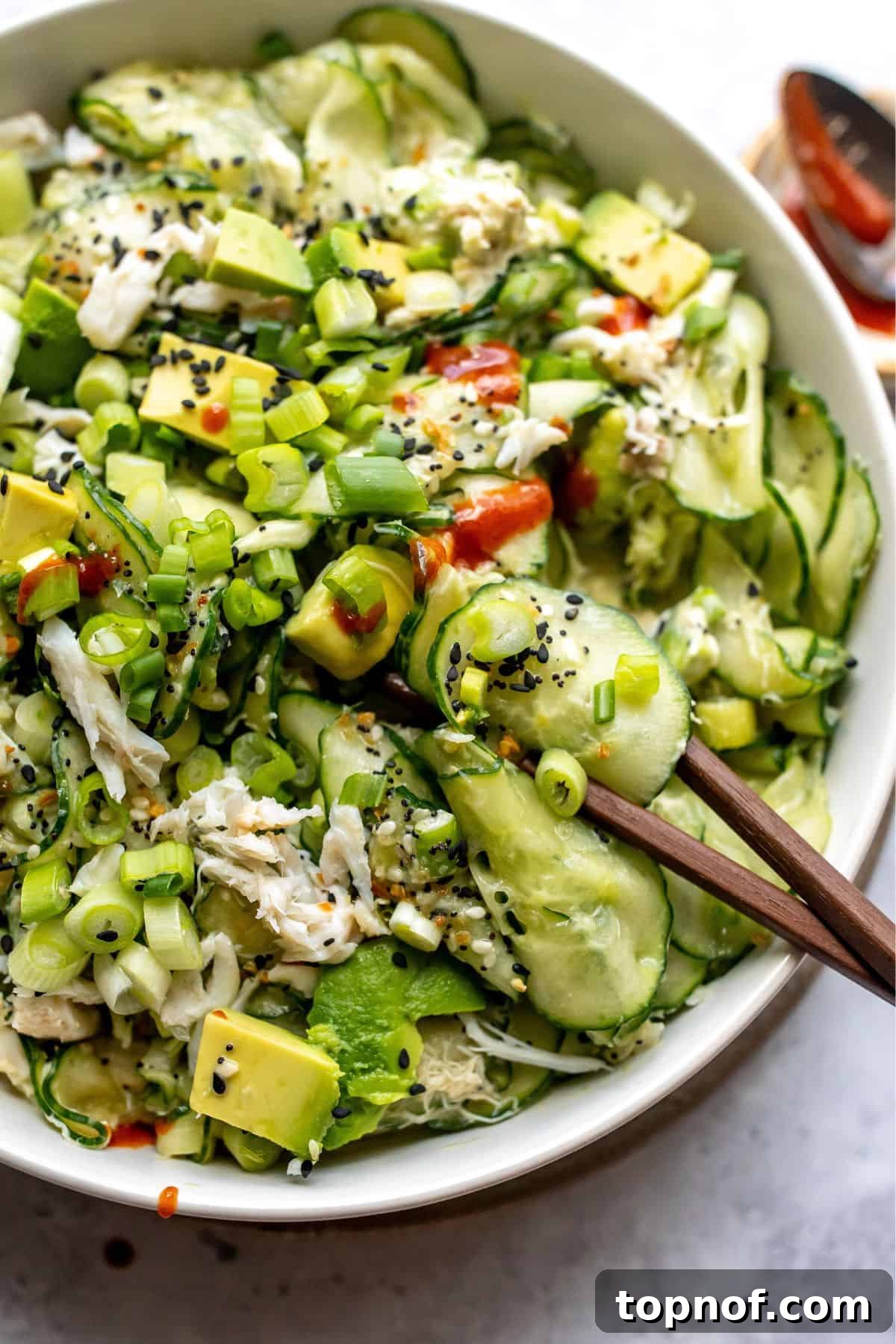 California Roll Cucumber Slaw 5 White bowl filled with California Roll Cucumber Salad with a drizzle of sriracha on top.