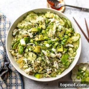 White bowl with filled with California Roll Cucumber Salad. Avocados on top with sesame seeds.