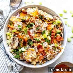 Smashed Buffalo Potato Salad in a white bowl with a silver spoon and a lemon on the side, ready to be served and enjoyed.
