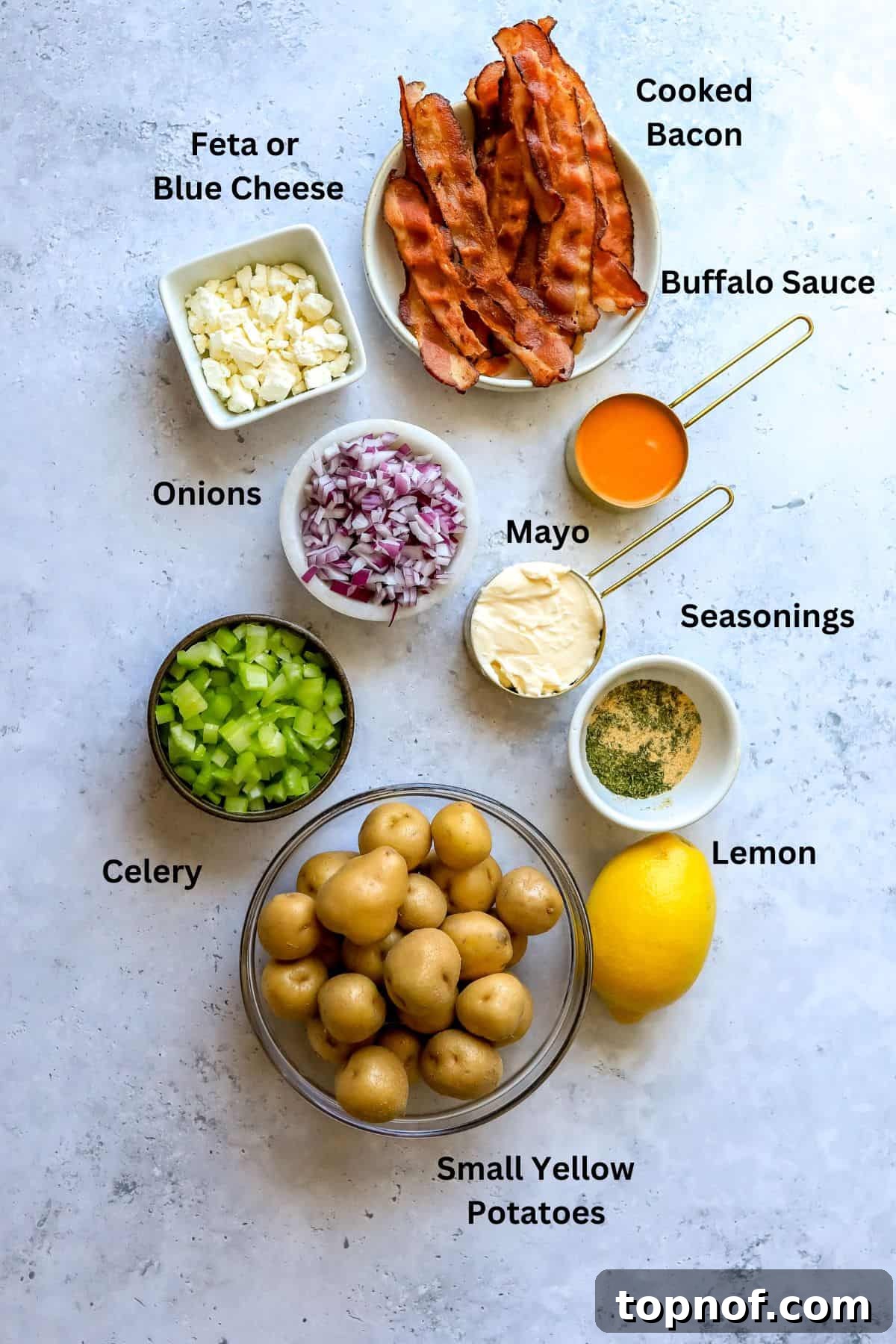 Buffalo Smashed Spud Salad 3 Ingredients for Smashed Buffalo Potato Salad neatly arranged in measuring cups on a grey countertop, including potatoes, fresh herbs, sauces, and cheese.