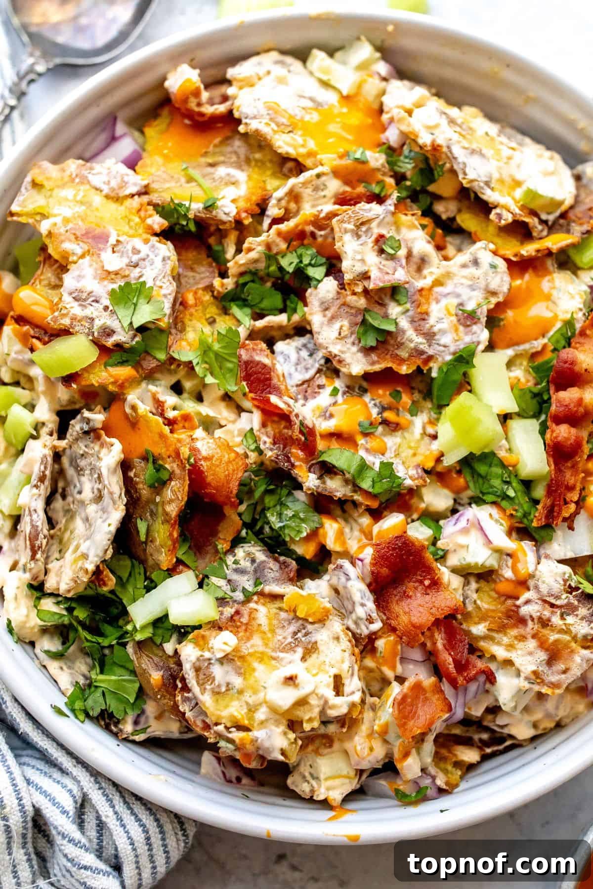 Buffalo Smashed Spud Salad 6 Smashed Buffalo Potato Salad in a white serving bowl, garnished with crispy bacon and a side of buffalo sauce, ready to be shared.