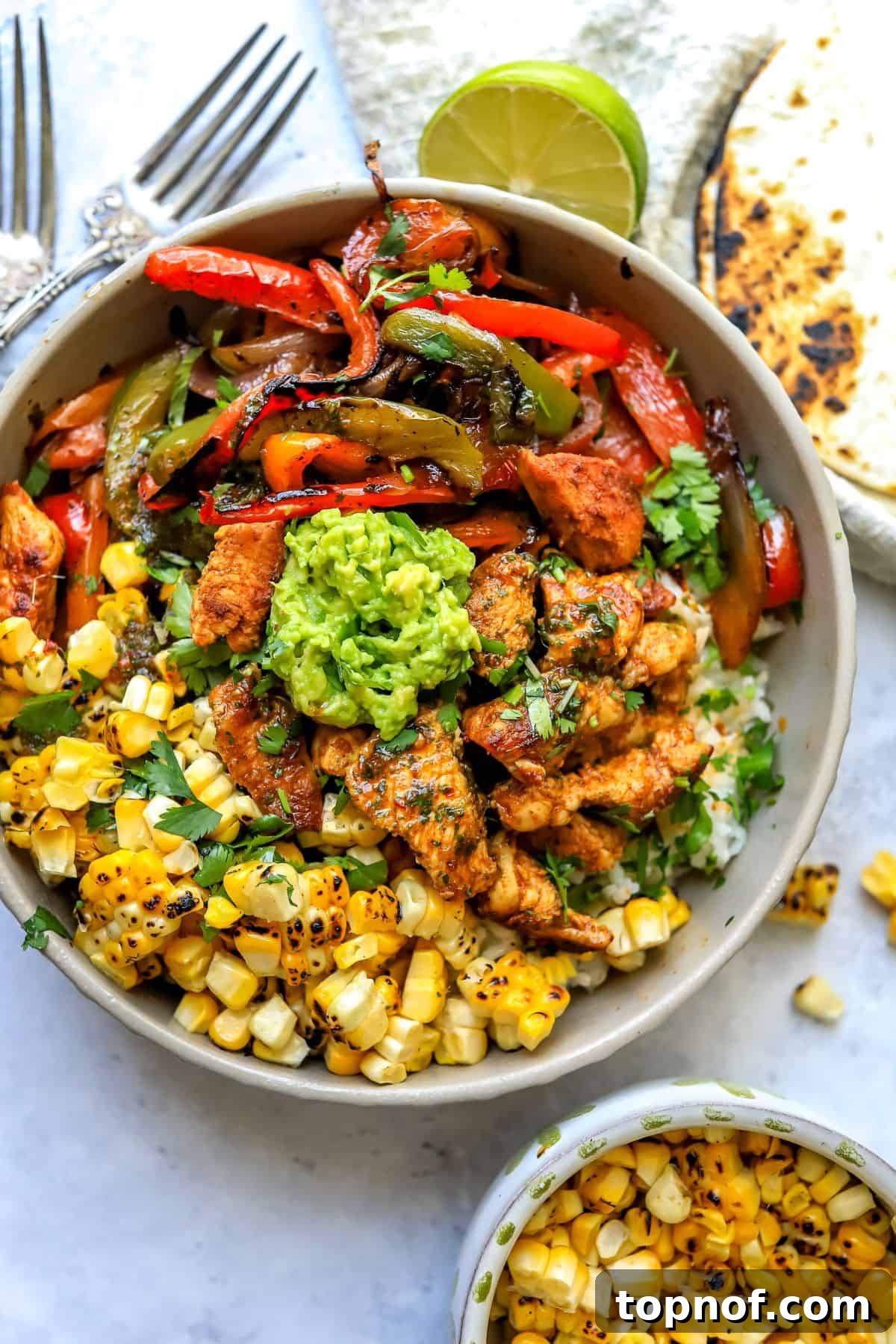A vibrant Chicken Fajita Bowl overflowing with seasoned chicken, colorful bell peppers, and fresh cilantro, served over rice with a dollop of guacamole.
